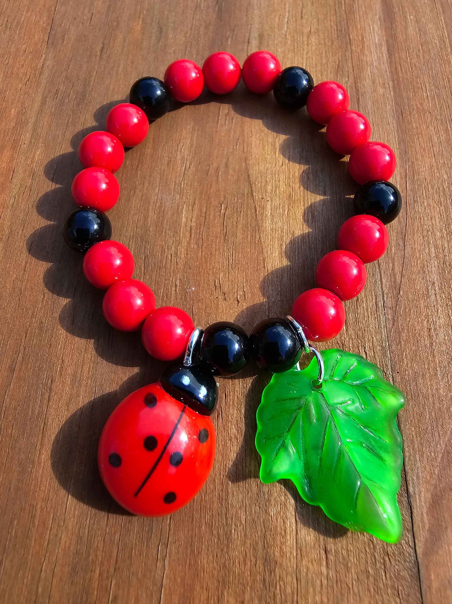 Kids ladybird bracelet, red and black beads with ladybird and leaf charm