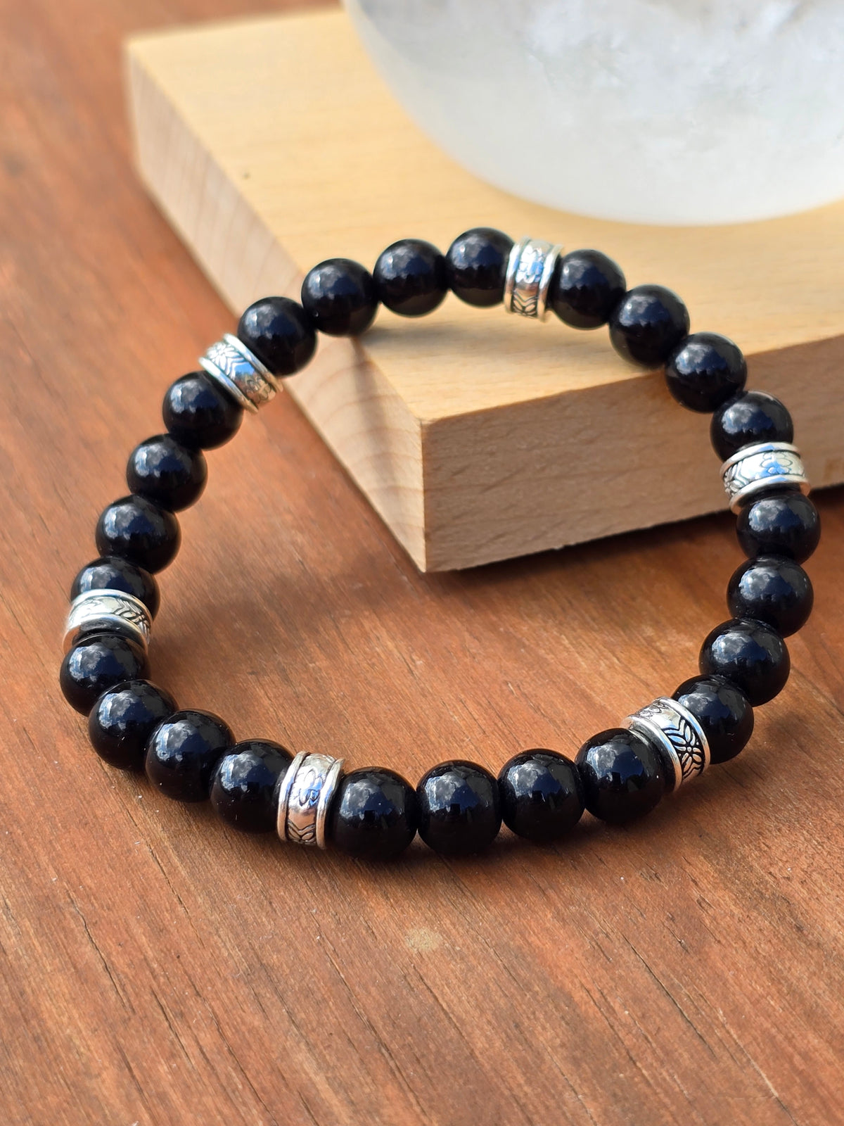 Glossy black stone beaded bracelet with engraved silver accent spacers displayed on a wooden surface.