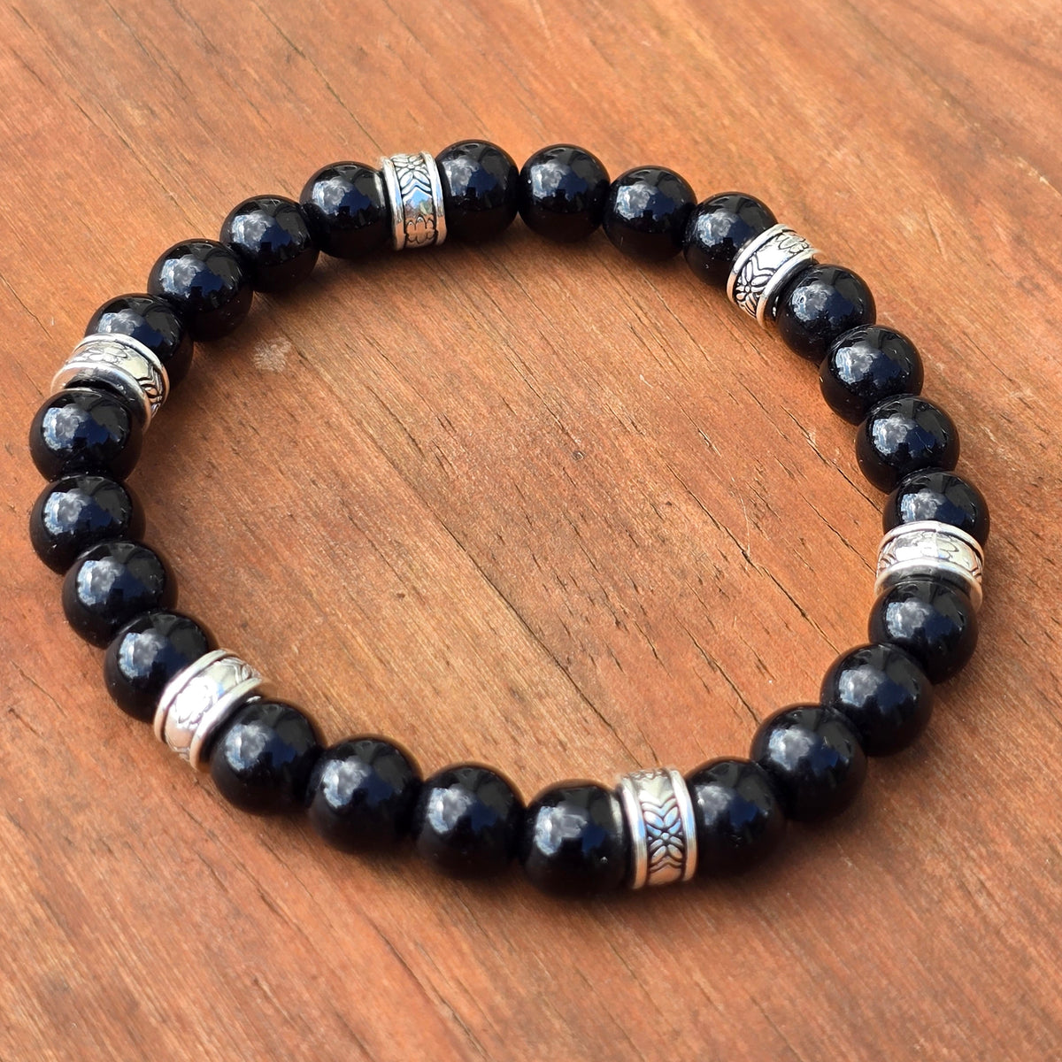 Glossy black stone beaded bracelet with engraved silver accent beads displayed on a wood surface.