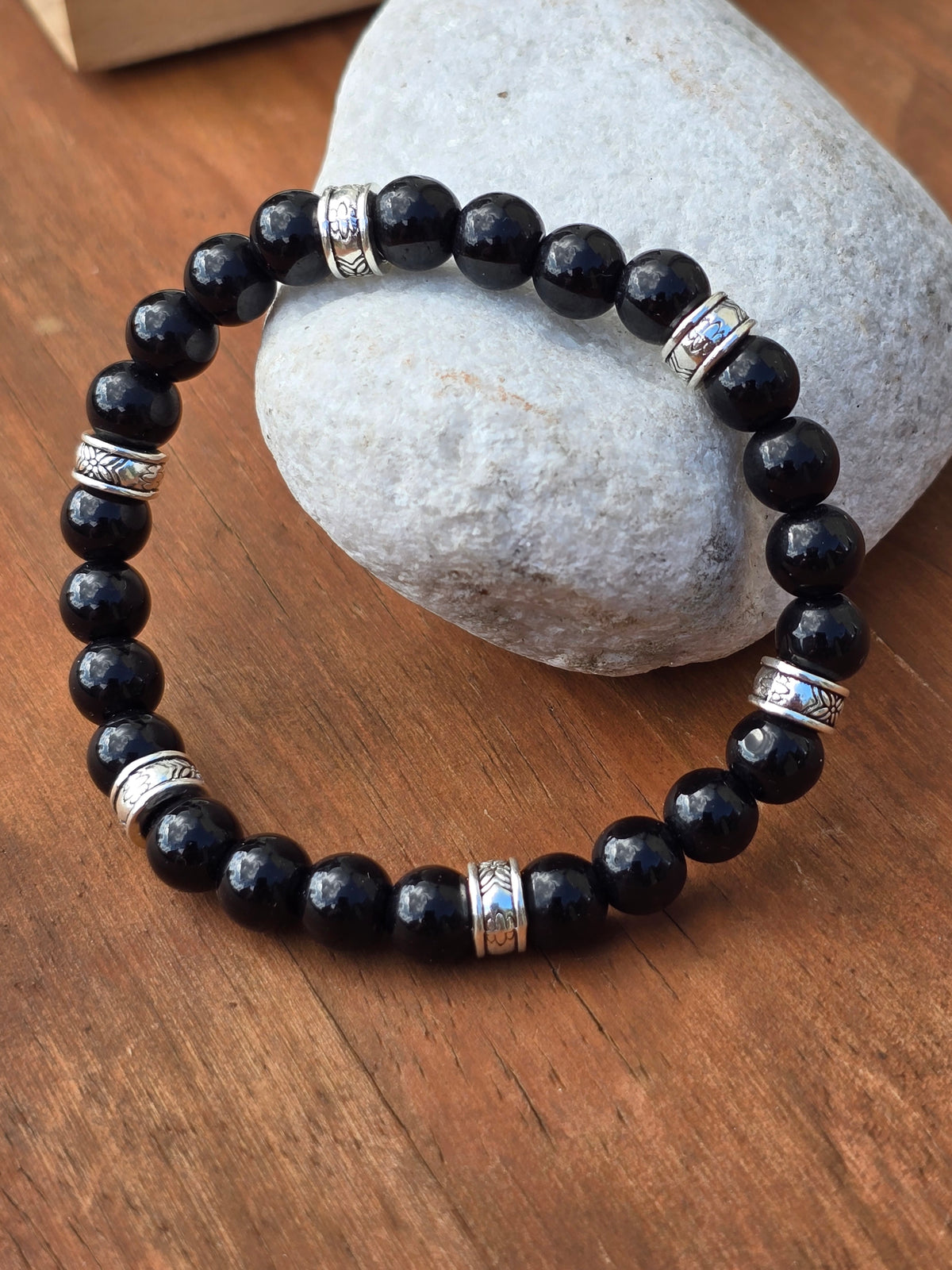 Glossy black stone beaded bracelet featuring engraved silver spacer rings on a wooden surface.