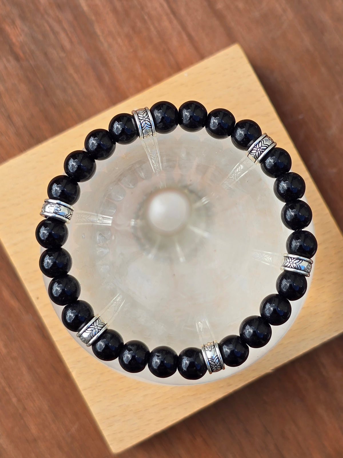 Glossy black stone beaded bracelet with engraved silver spacers resting on an upturned glass.