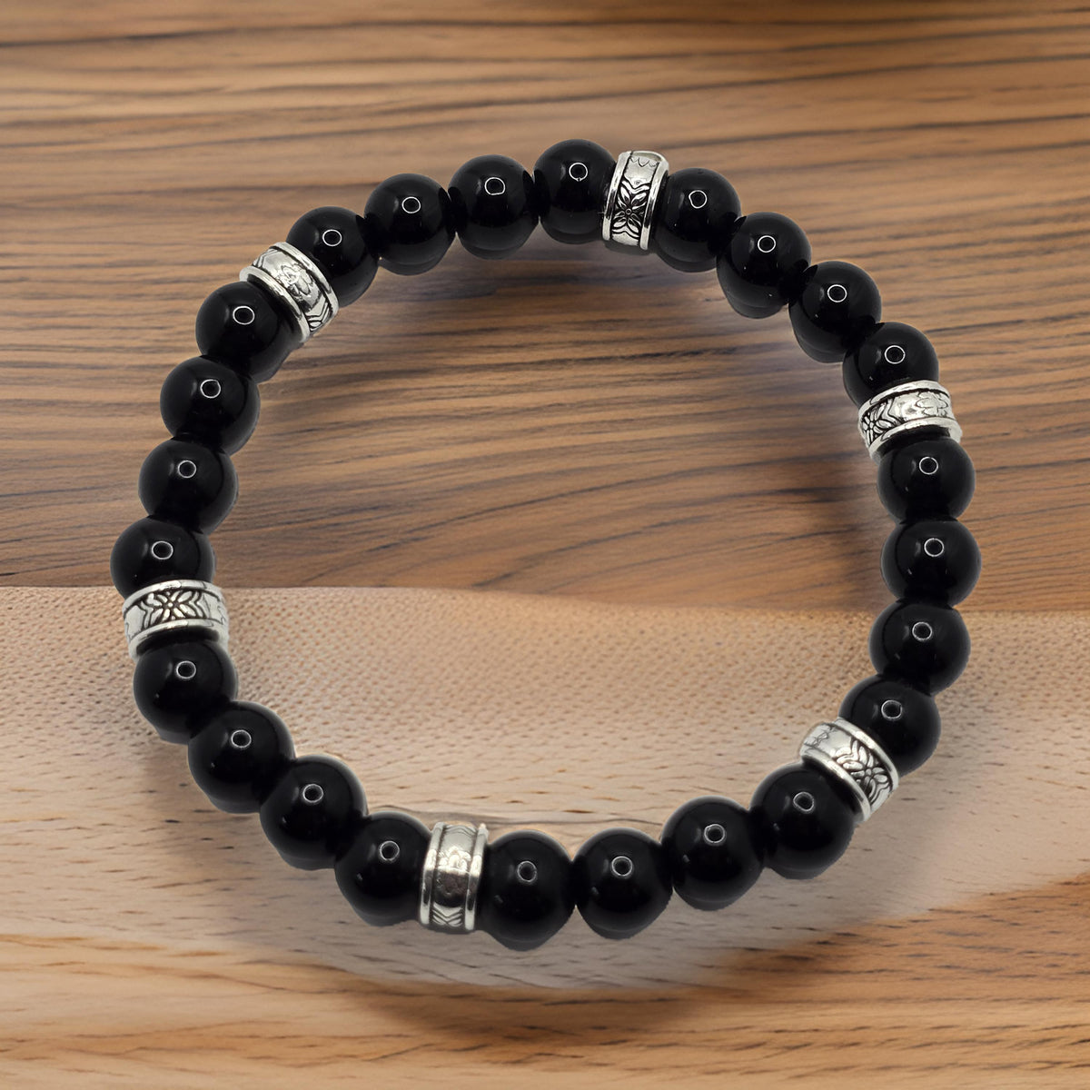 Glossy black stone beaded bracelet with ornate silver accent rings on a wooden surface.