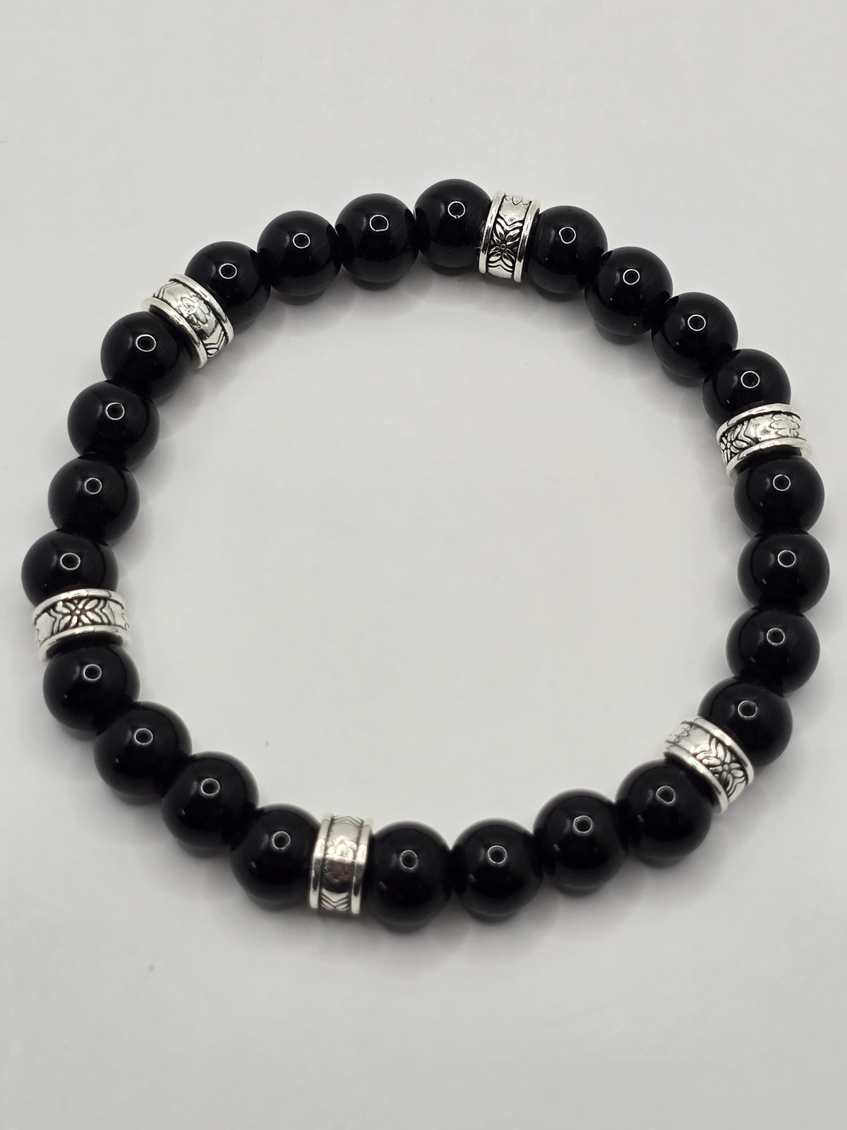 Glossy black beaded bracelet accented with engraved silver spacer rings on a white background.
