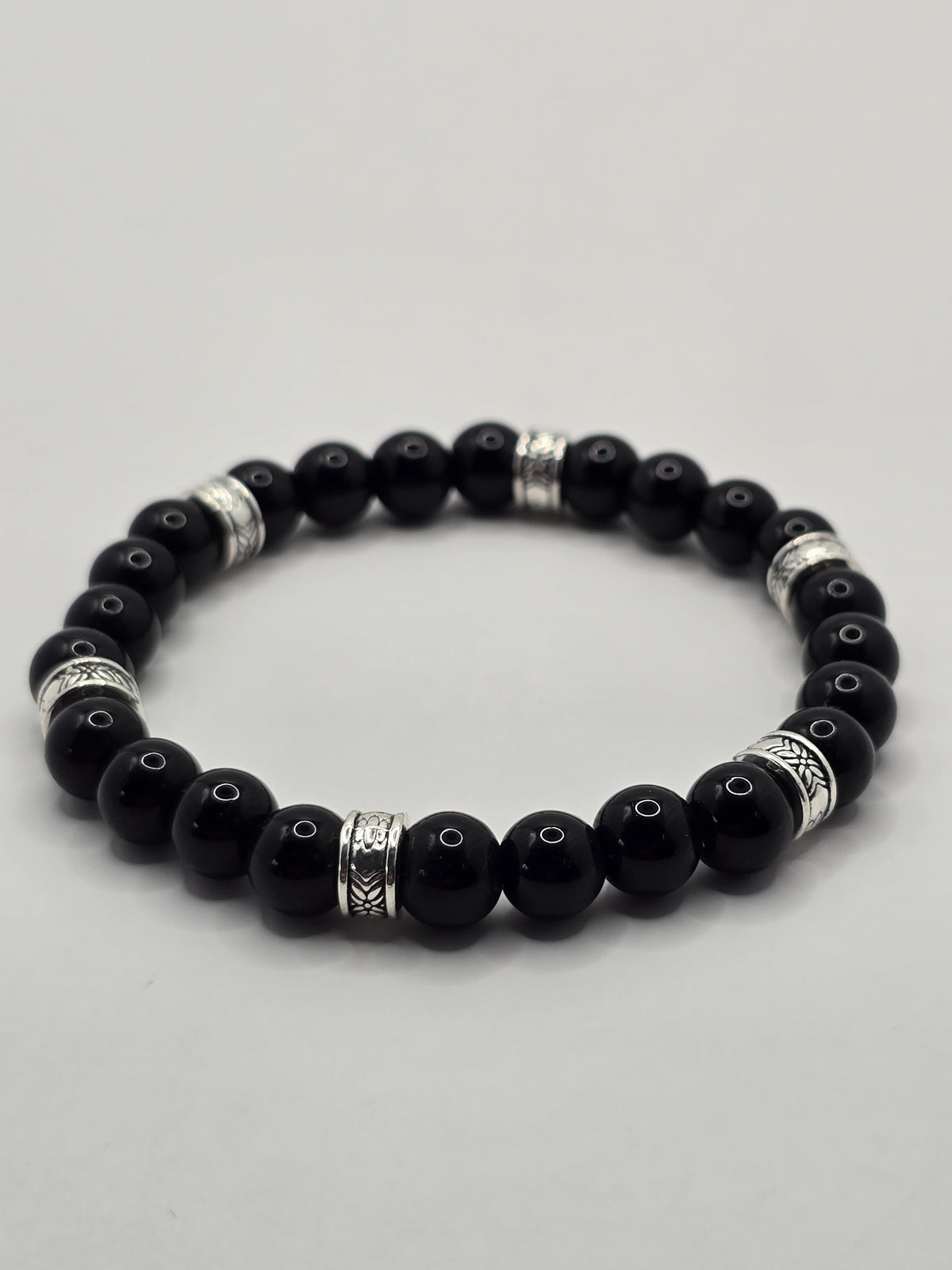 Glossy black stone beaded bracelet with ornate silver spacer accents on a white surface.