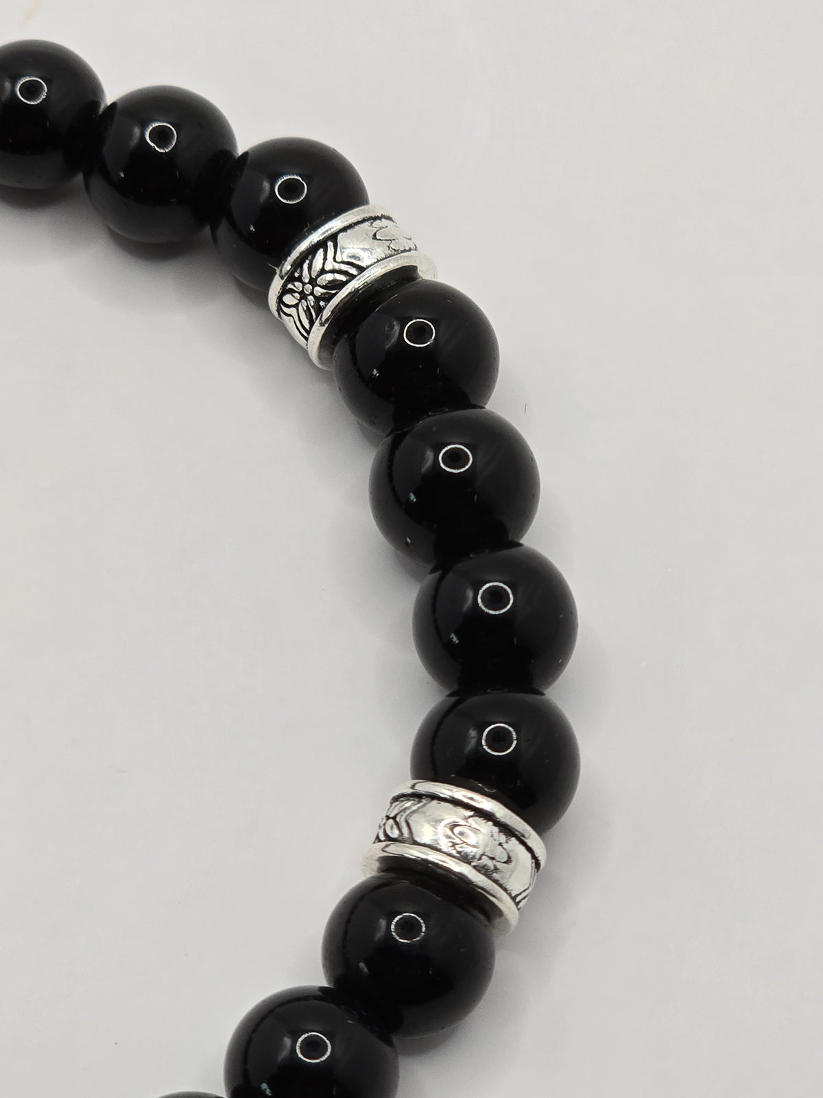 Close-up of a glossy black stone bead bracelet with patterned silver spacer accents.