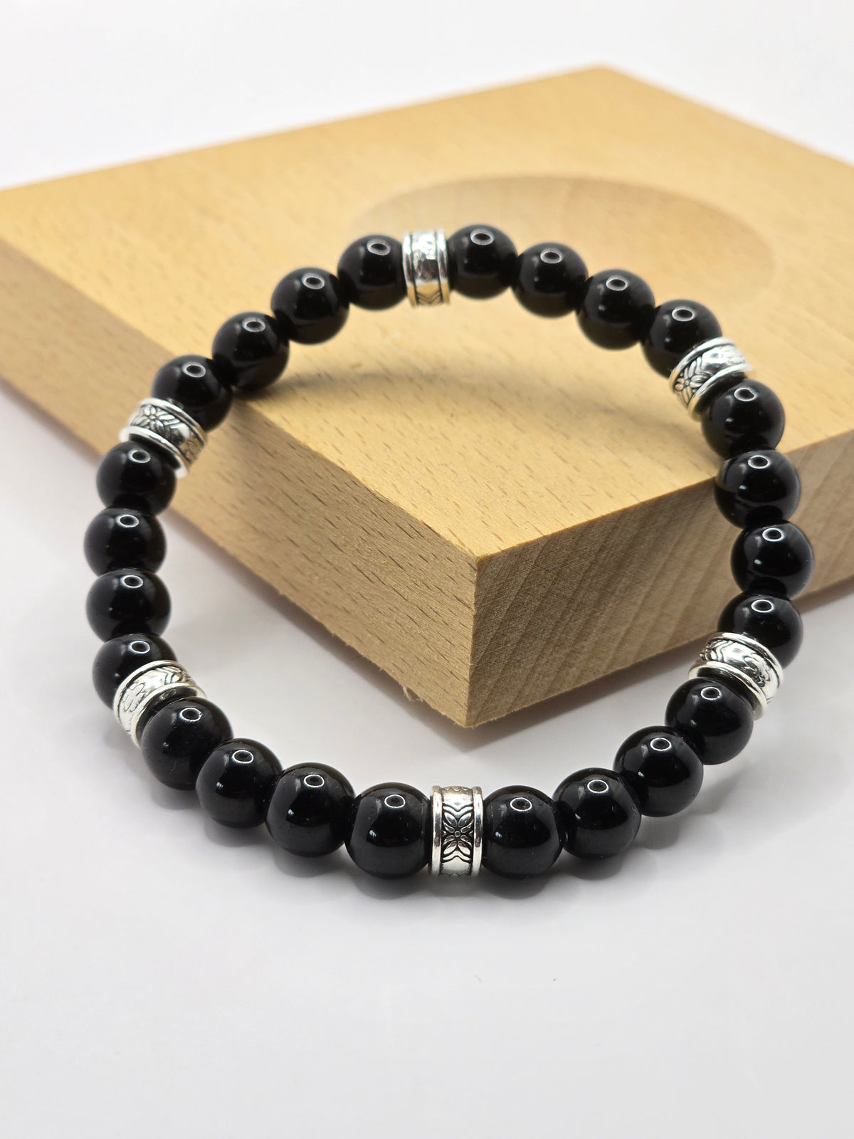 Glossy black beaded bracelet featuring patterned silver accent spacers, resting against a wooden block.