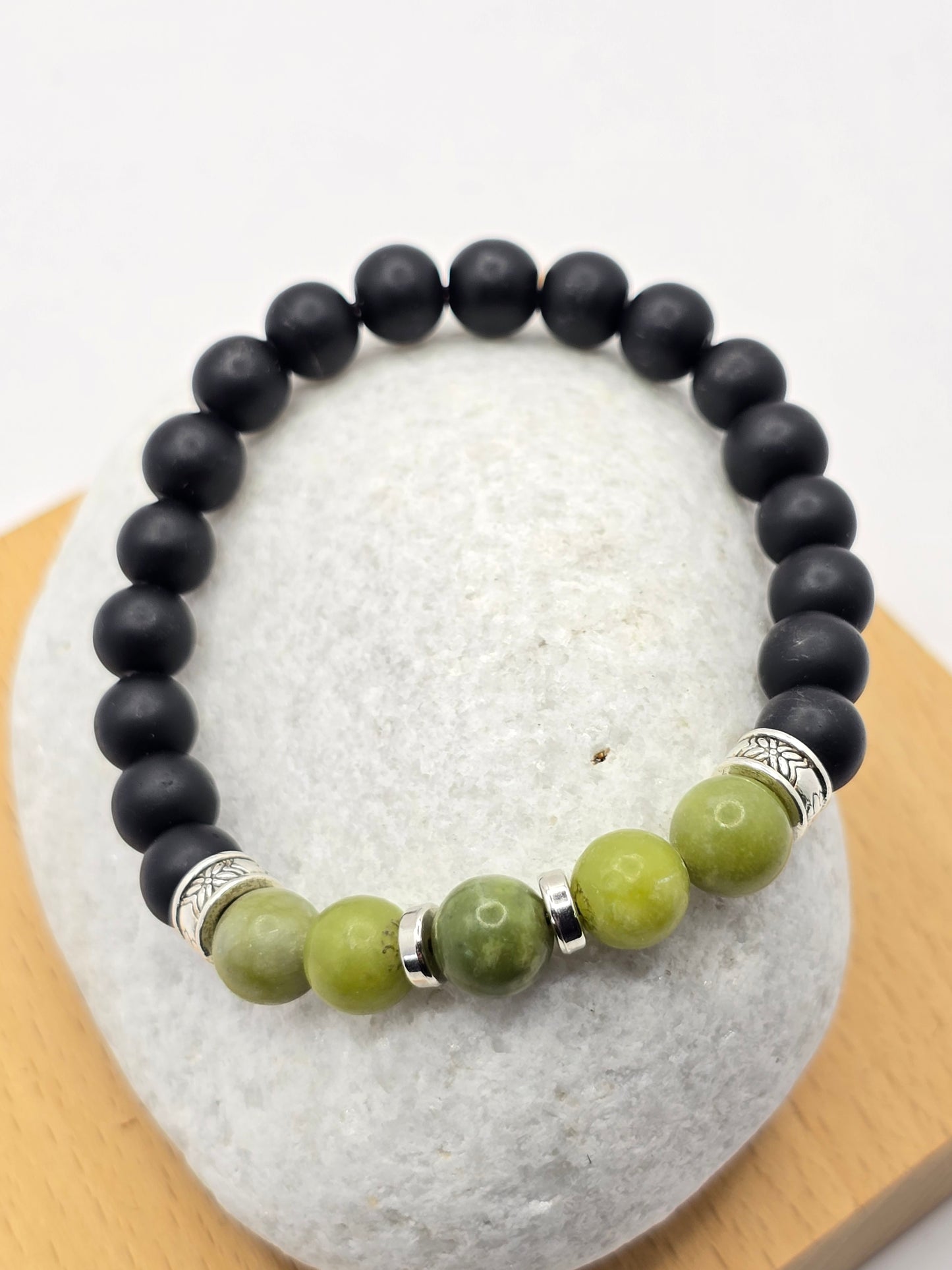 green and black stone beaded bracelet, displayed on a large white pebble.