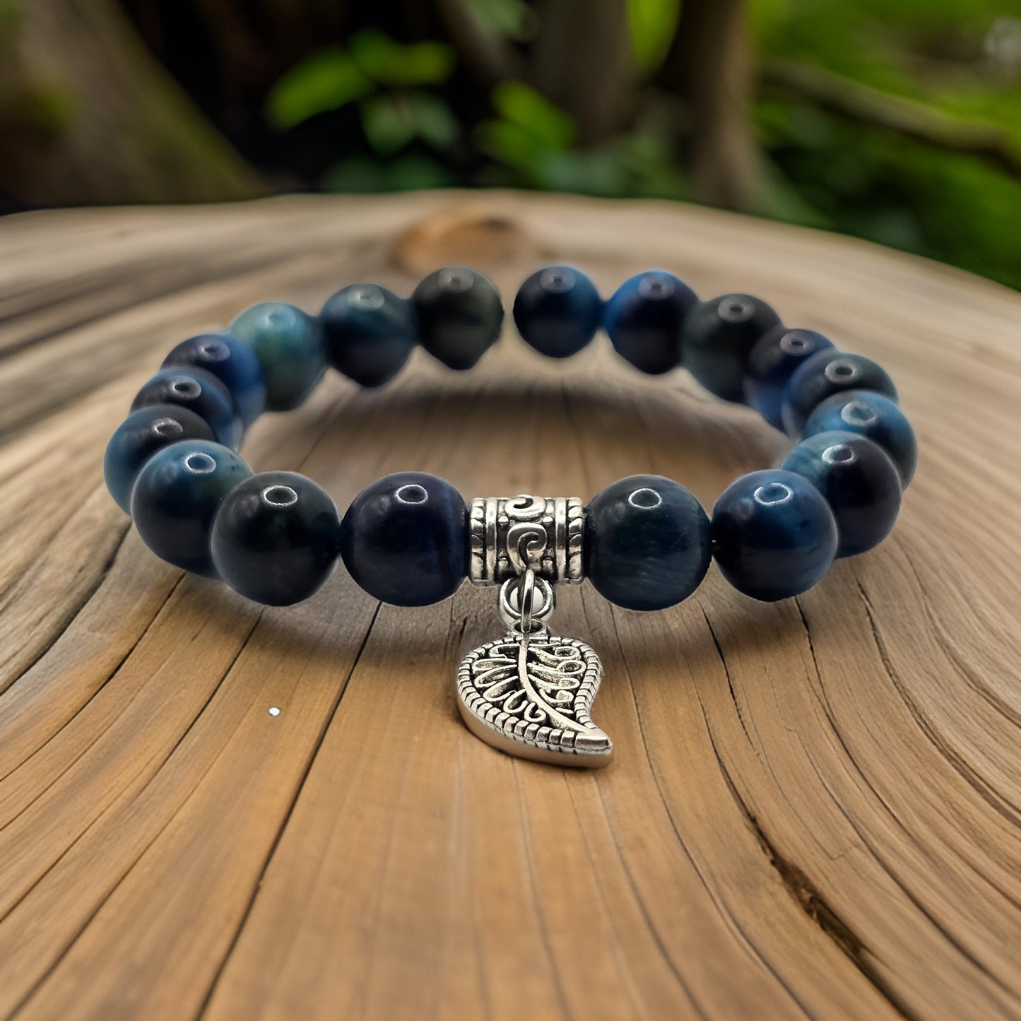 Women's blue beaded elasticated bracelet with leaf motif resting on a tree trunk