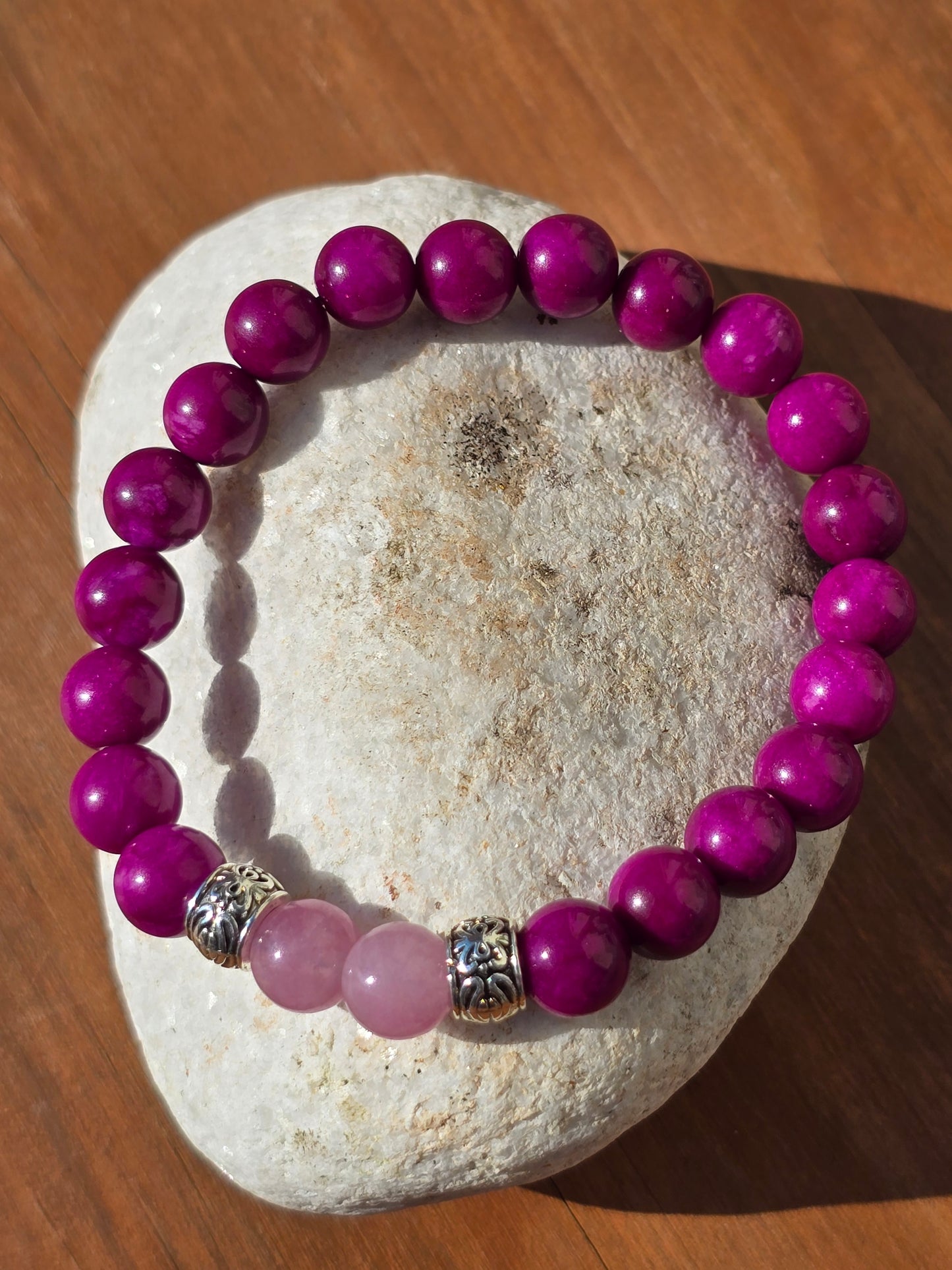 Purple beaded bracelet with a silver clasp on a stone surface