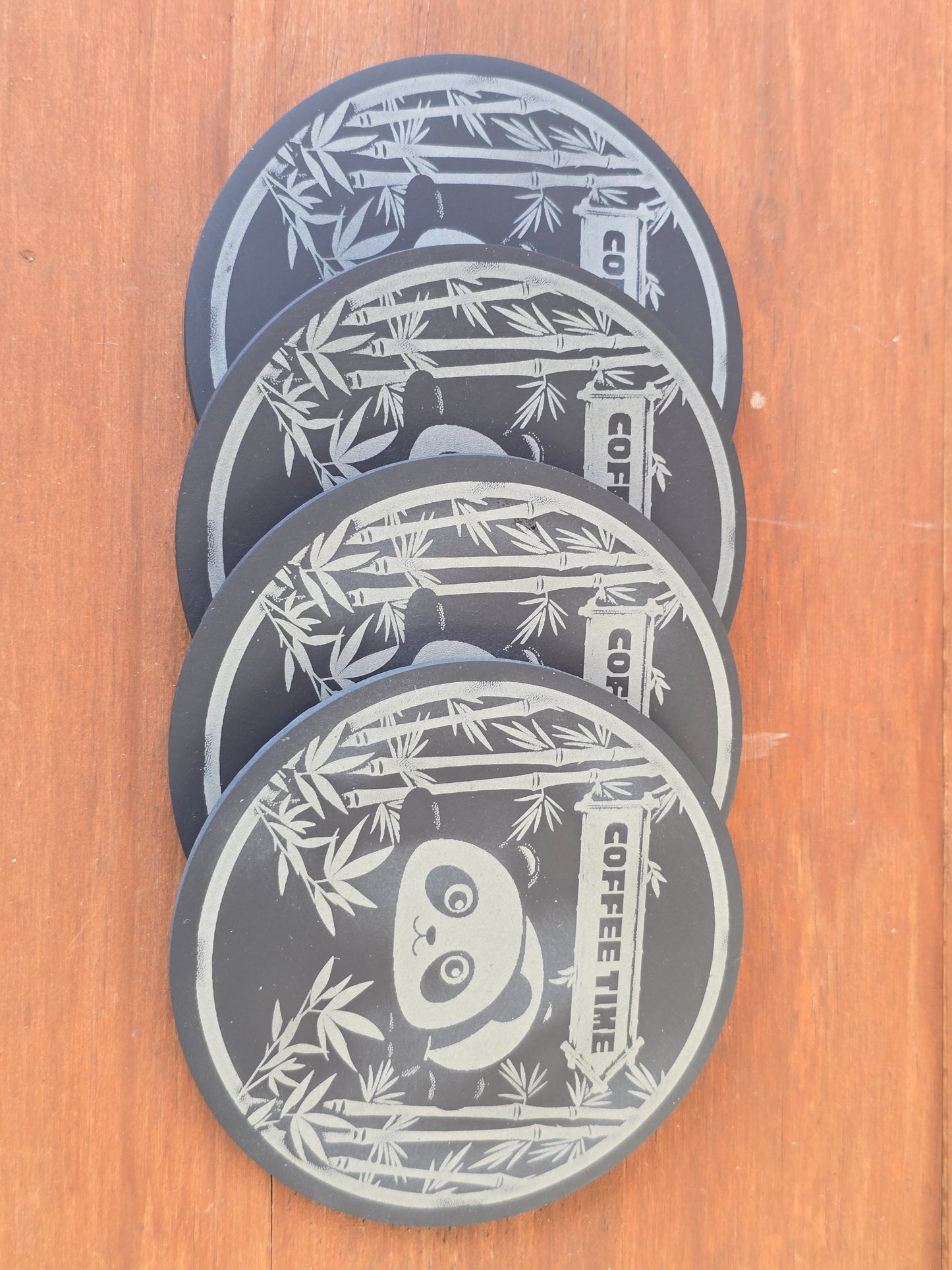 Set of four black coasters with panda design and 'Coffee Time' text on a wooden surface