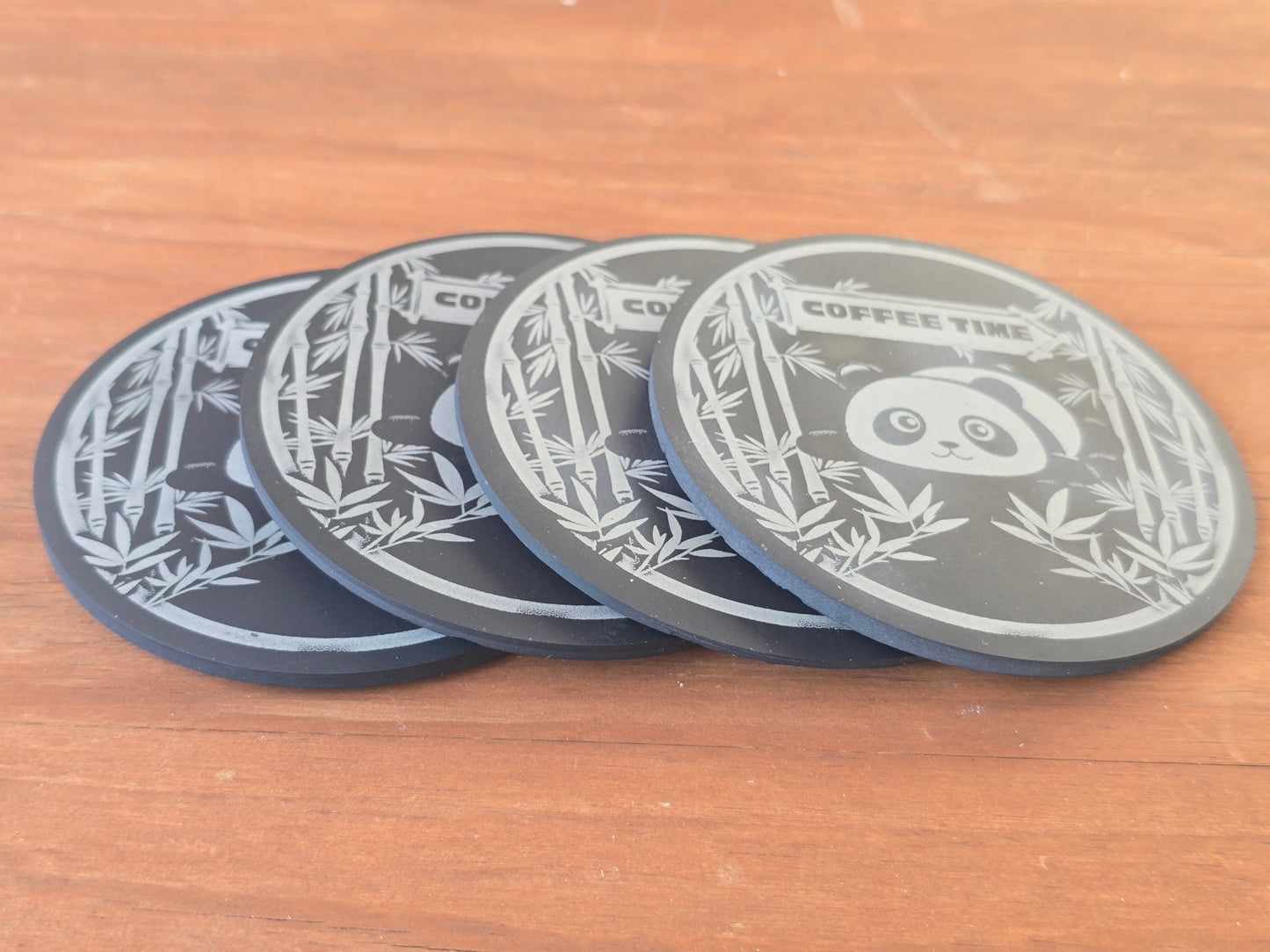 Four black coasters with lying panda and bamboo designs on a wooden surface