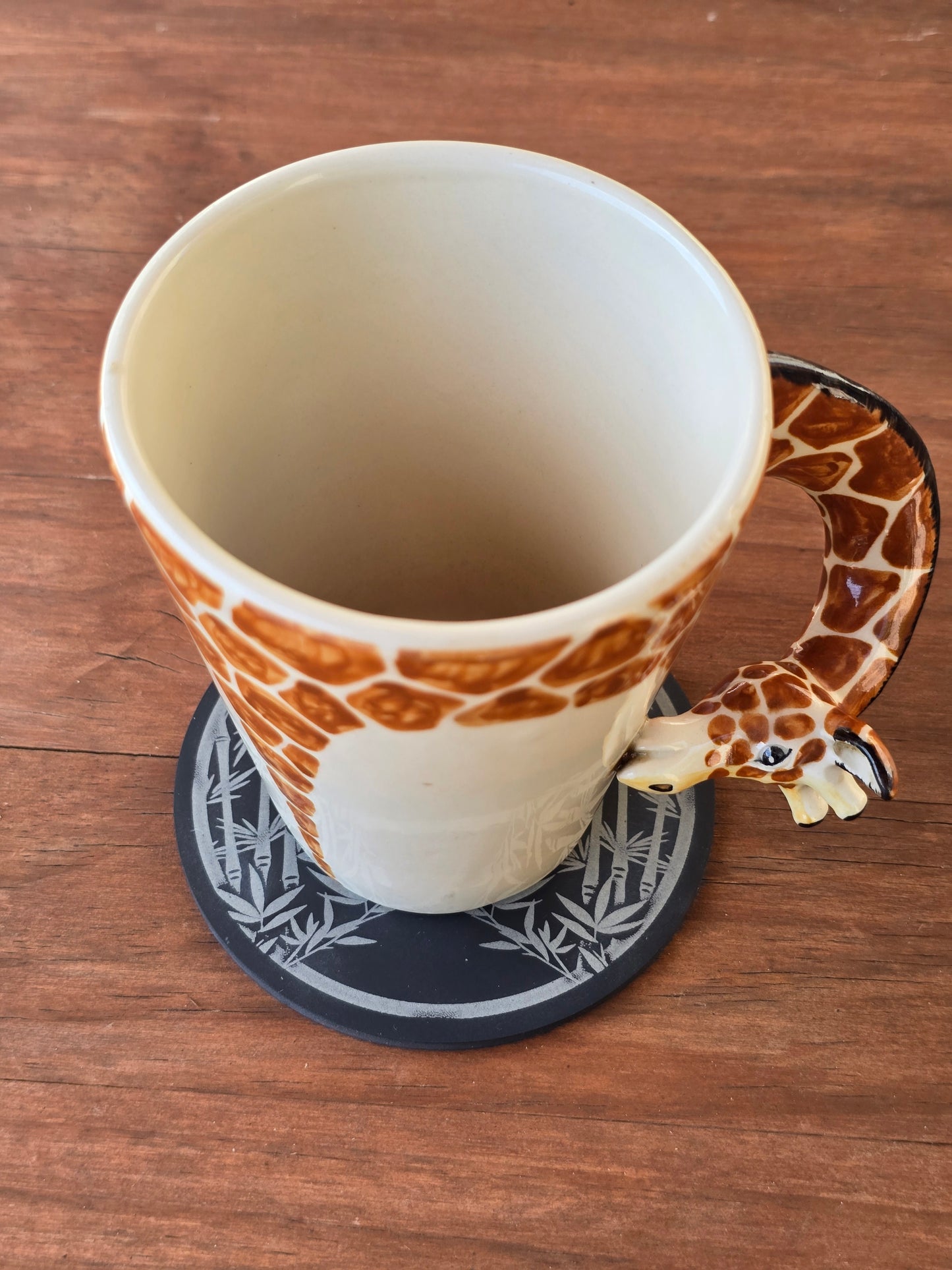 Giraffe-shaped mug on a wooden surface with a slate panda coaster underneath