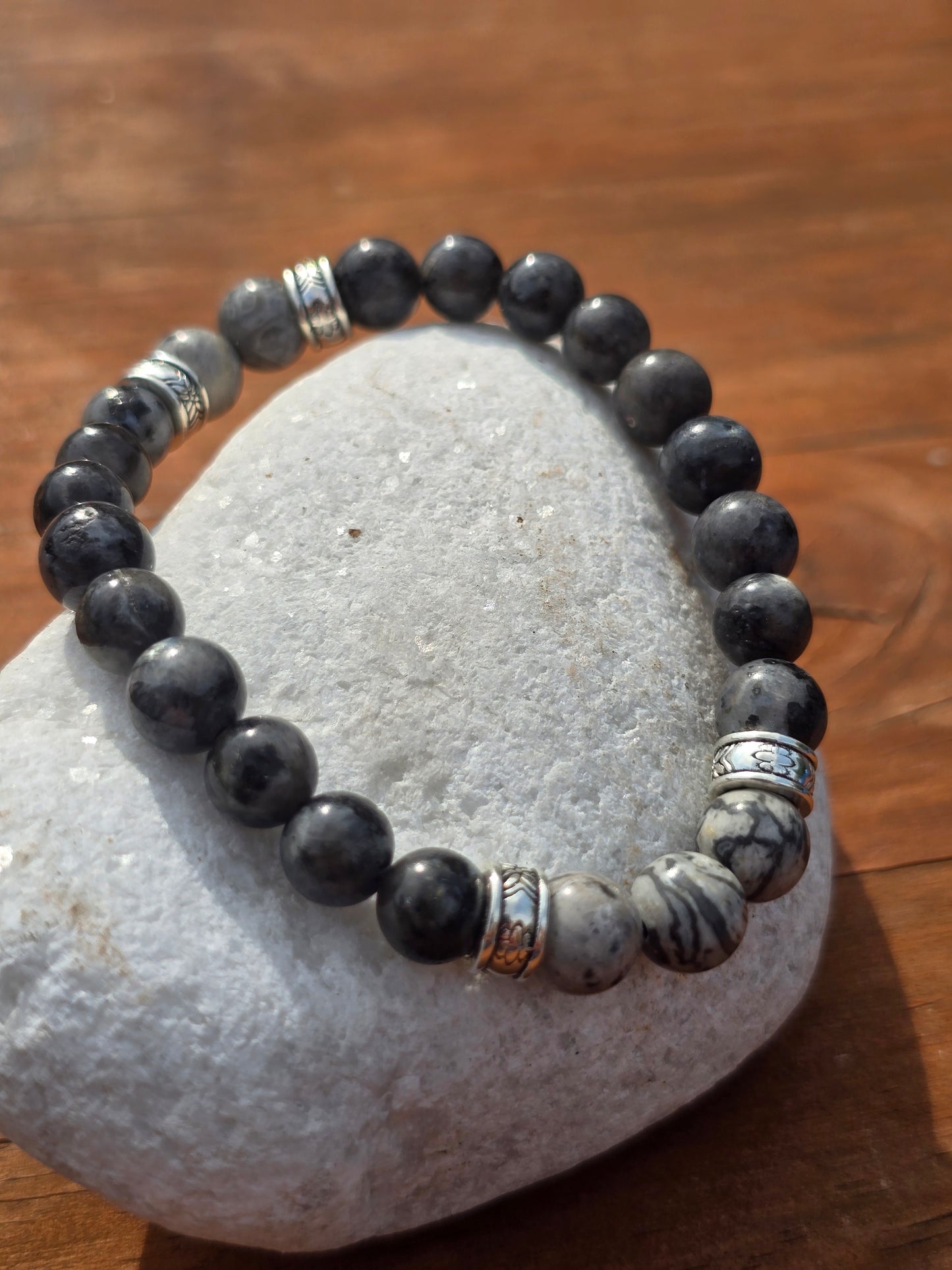 Grey beaded bracelet with silver accents on a stone surface