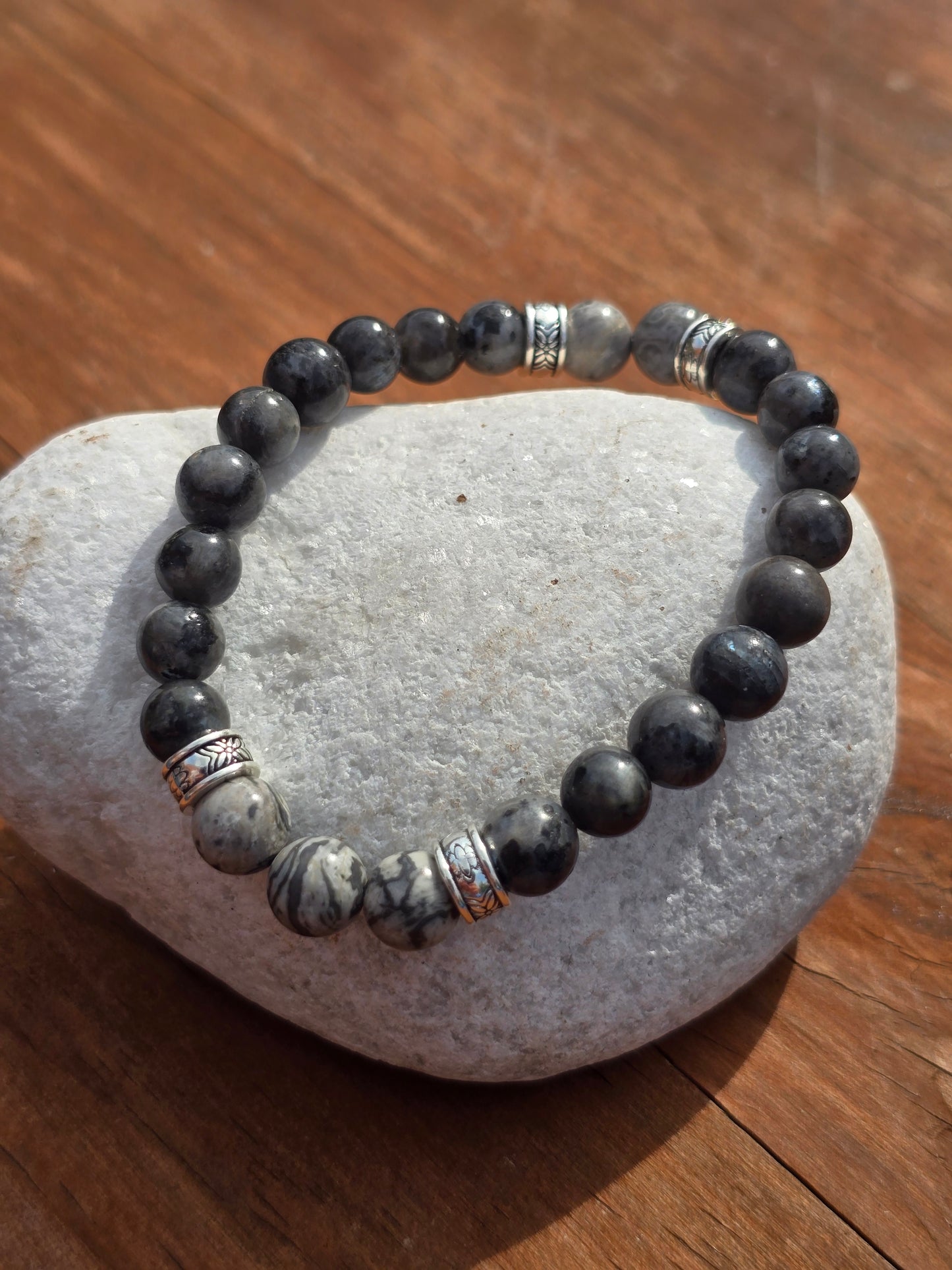 Grey beaded bracelet with silver accents on a white stone pebble
