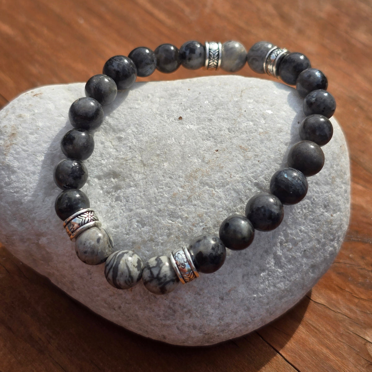Grey beaded bracelet with marble effect and silver accents displayed on a white stone pebble