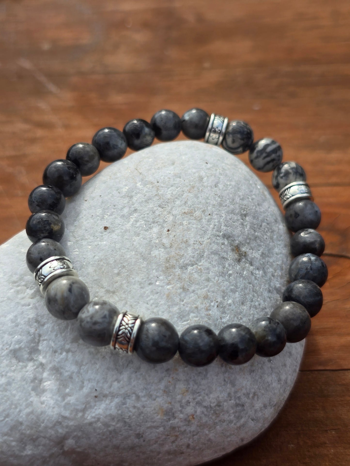 mens grey beaded bracelet with silver accents on a stone surface
