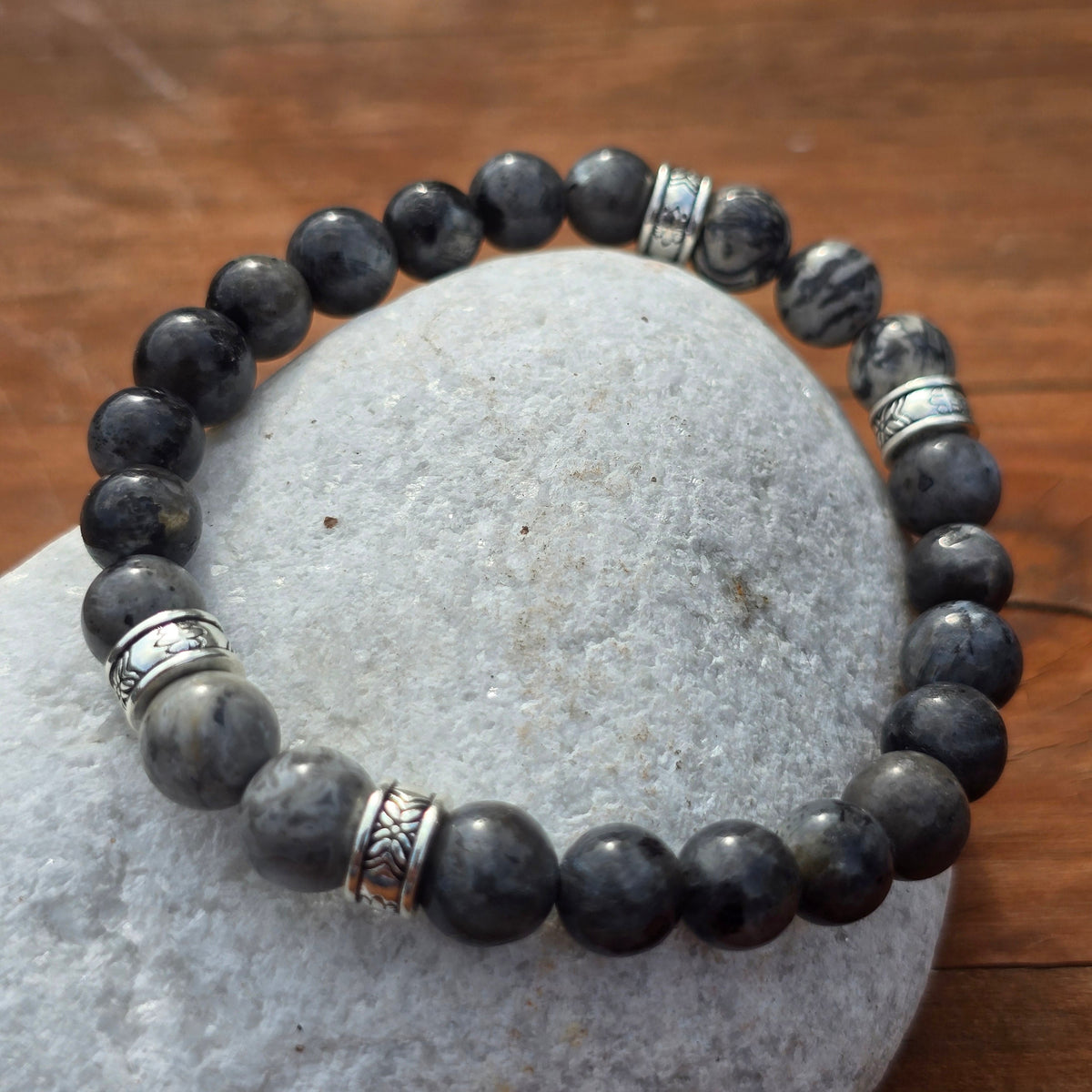 men's grey stone beaded bracelet with silver accents on a stone surface