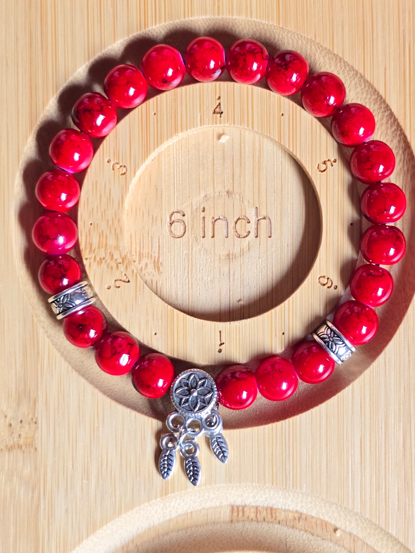 Red beaded bracelet with silver charms on a wooden measurement tool showing a 6 inch size