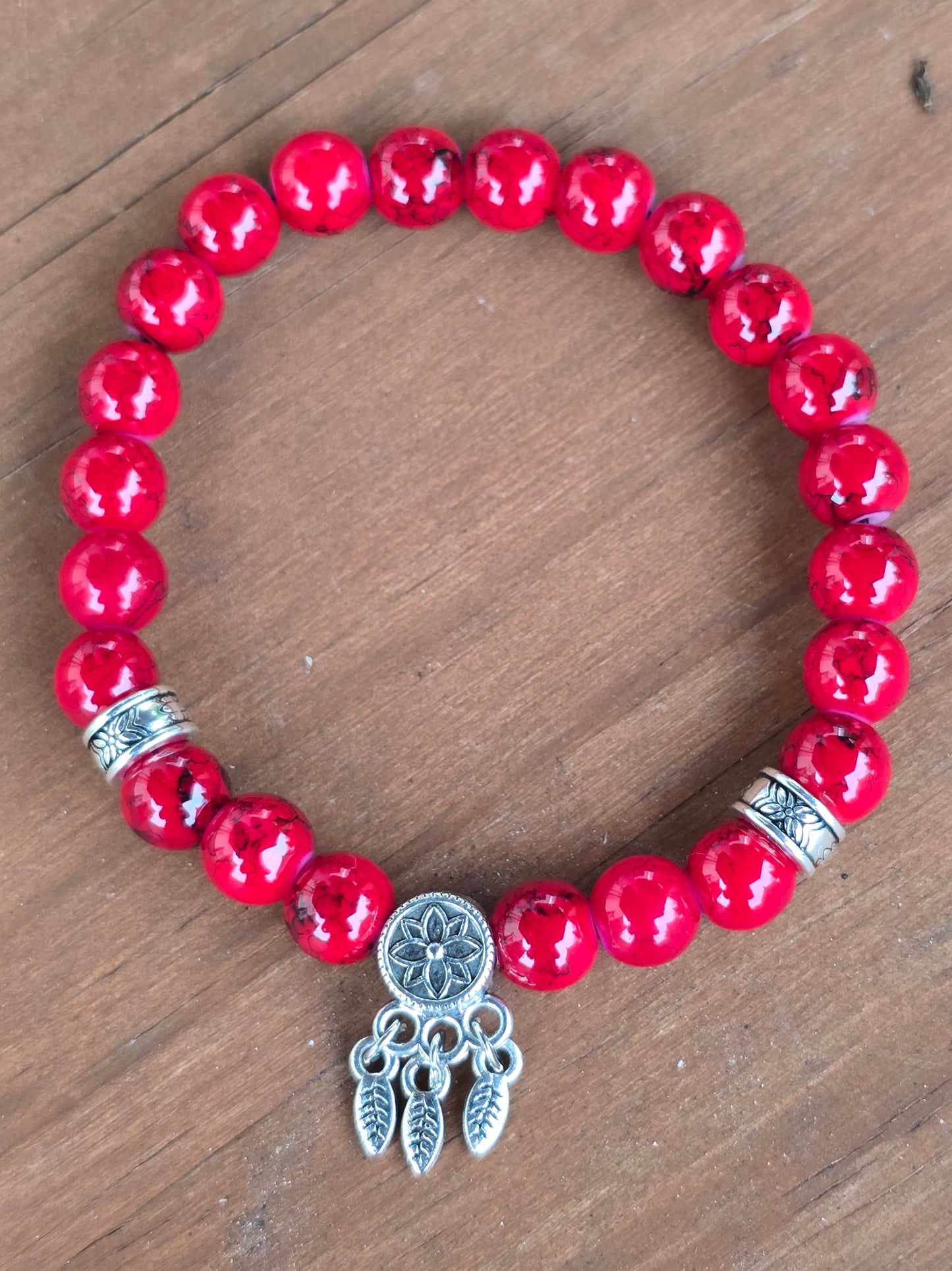 Red beaded bracelet with a silver dreamcatcher charm on a wooden background