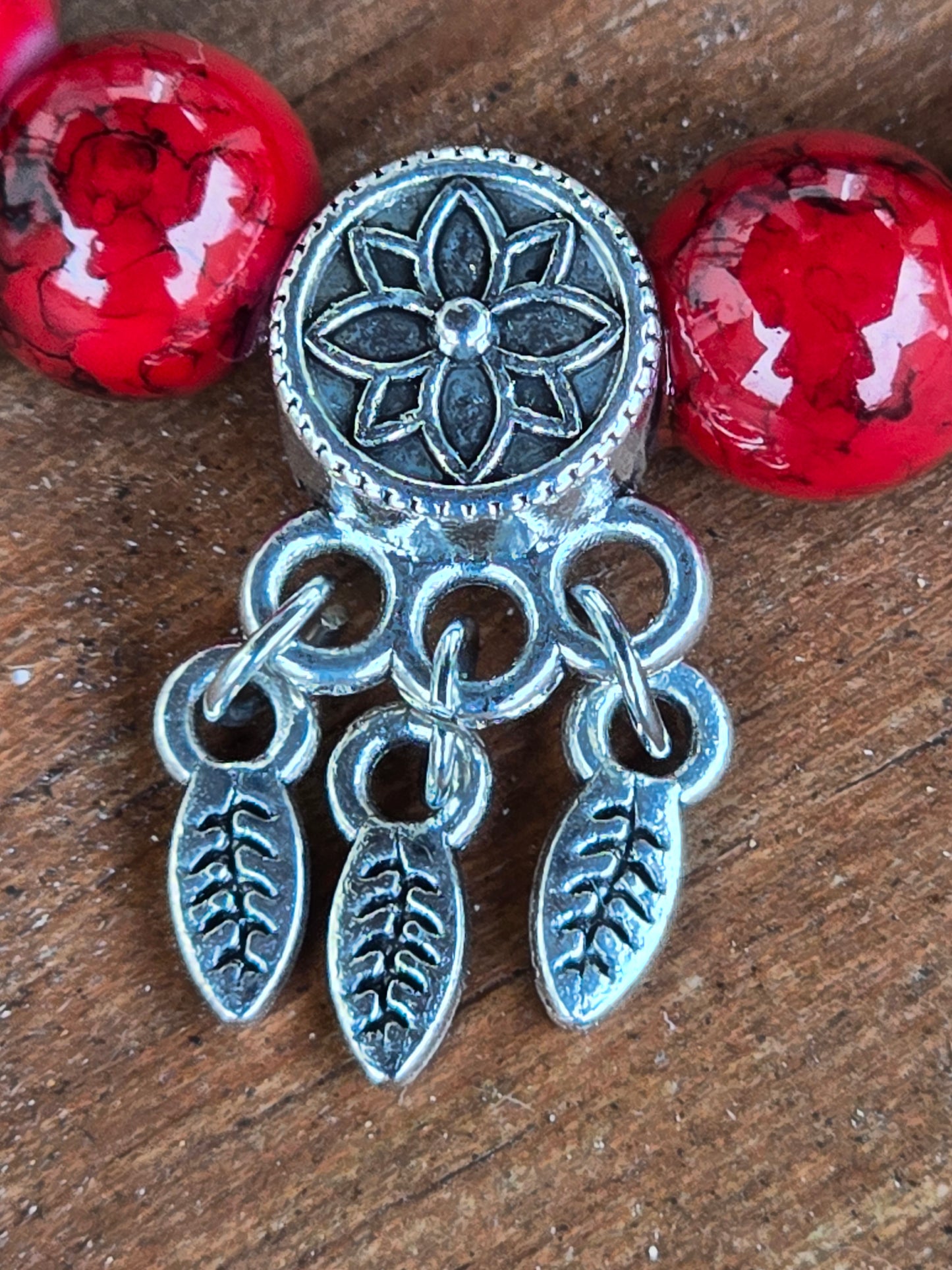 Silver decorative dreamcatcher element with floral design on a wooden surface