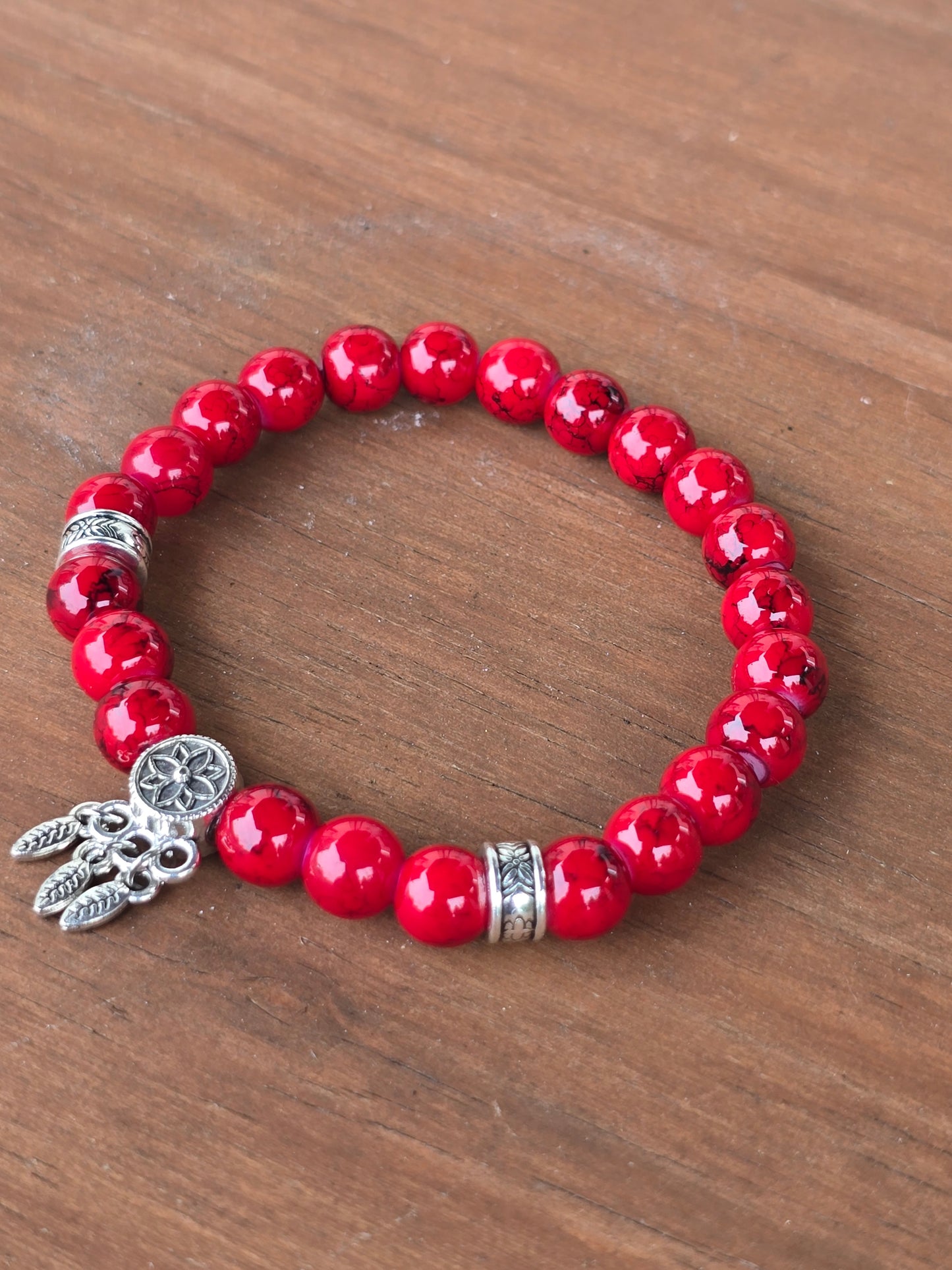 Red beaded bracelet with silver charms on a wooden surface