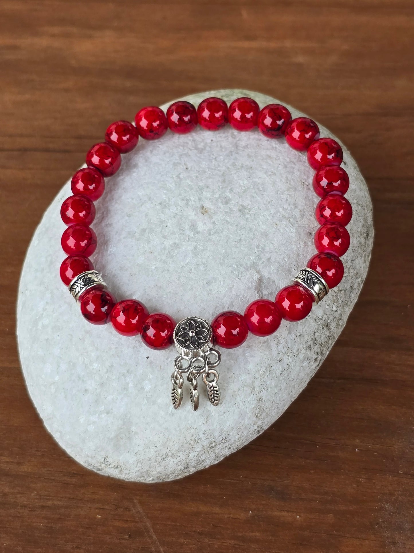 Shiny Red beaded bracelet with a silver charm on a stone surface