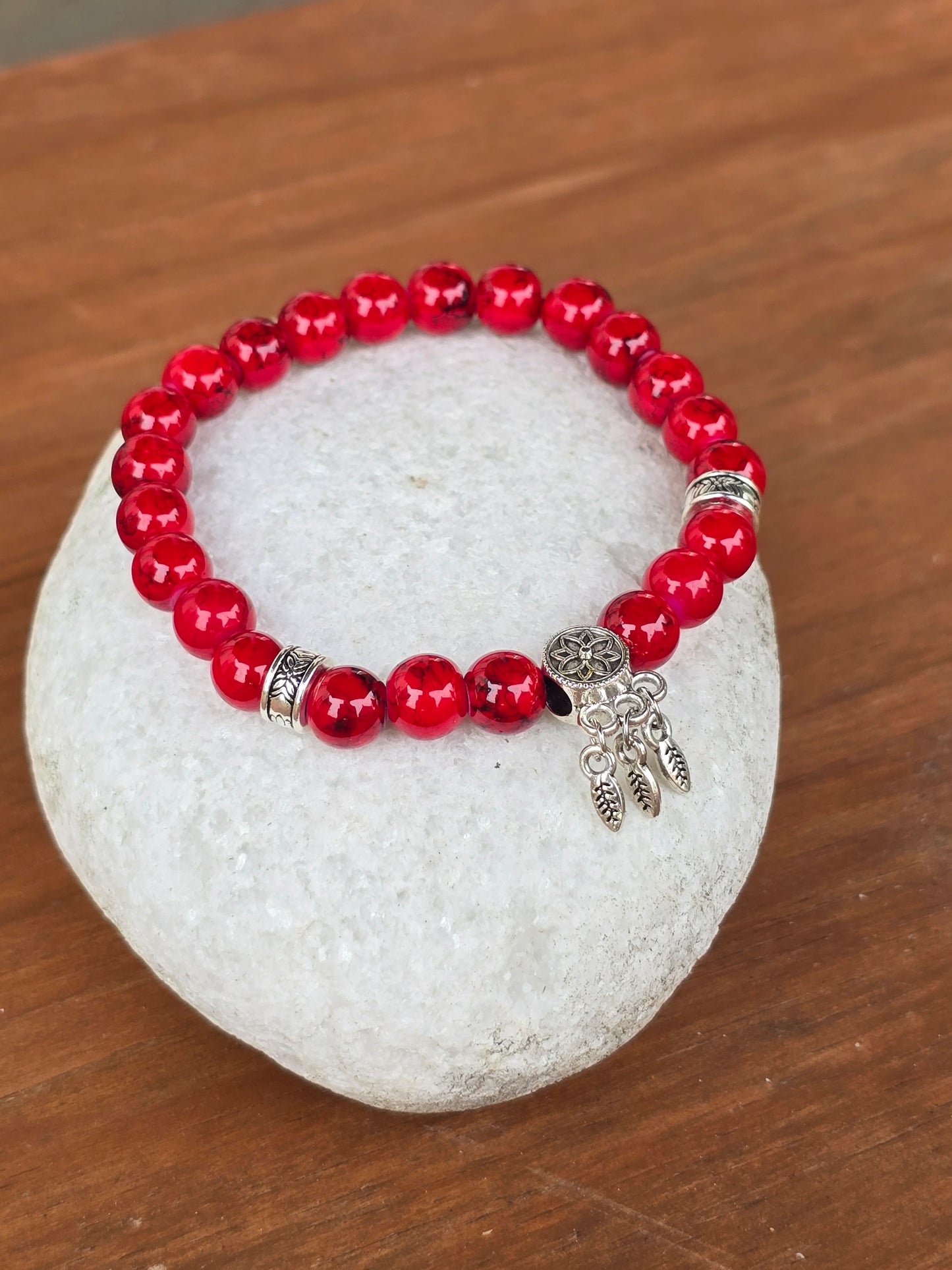 Red glossy beaded bracelet with a silver charm sitting on a white stone