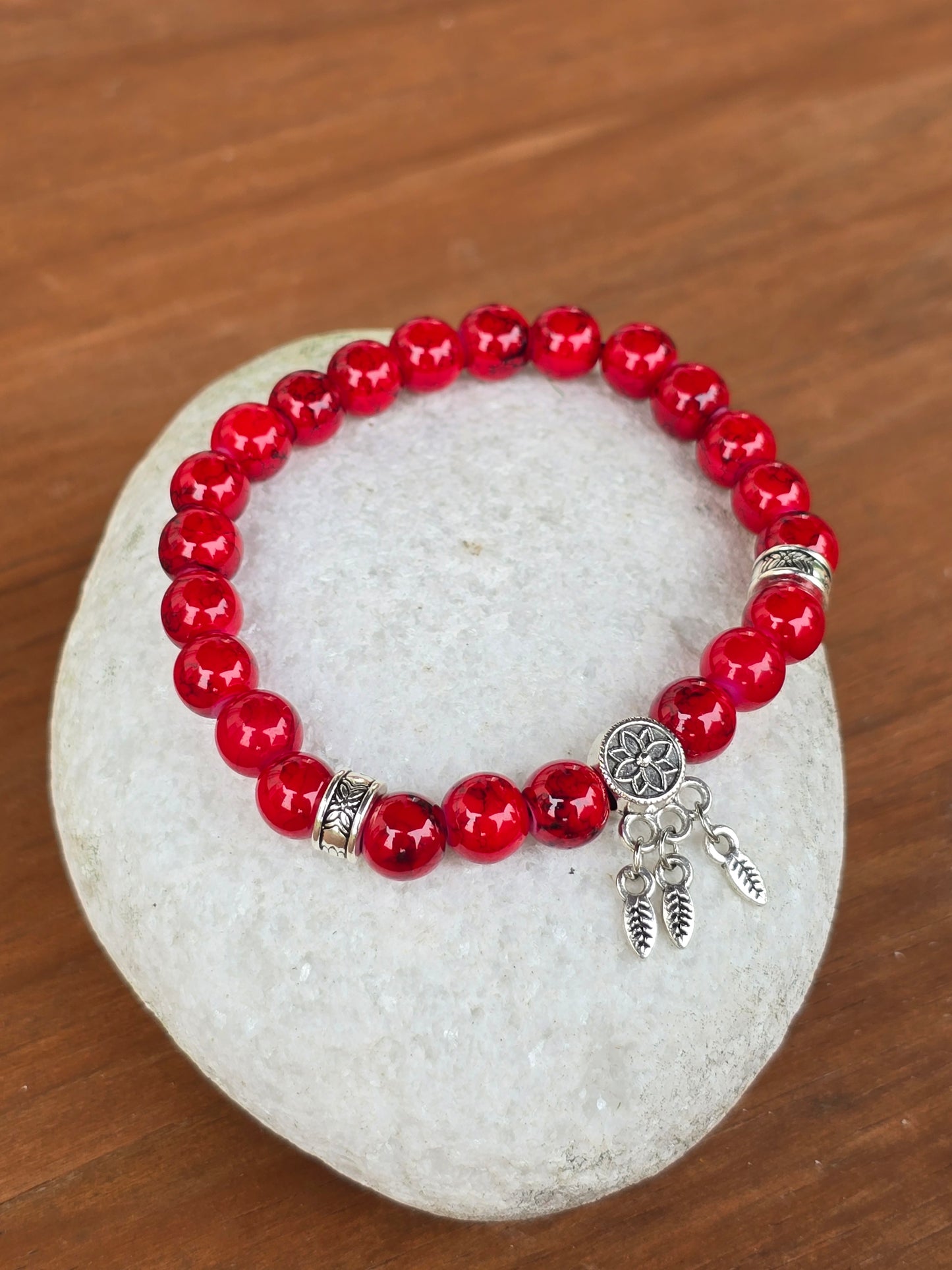 Red beaded bracelet with silver charms on a white stone