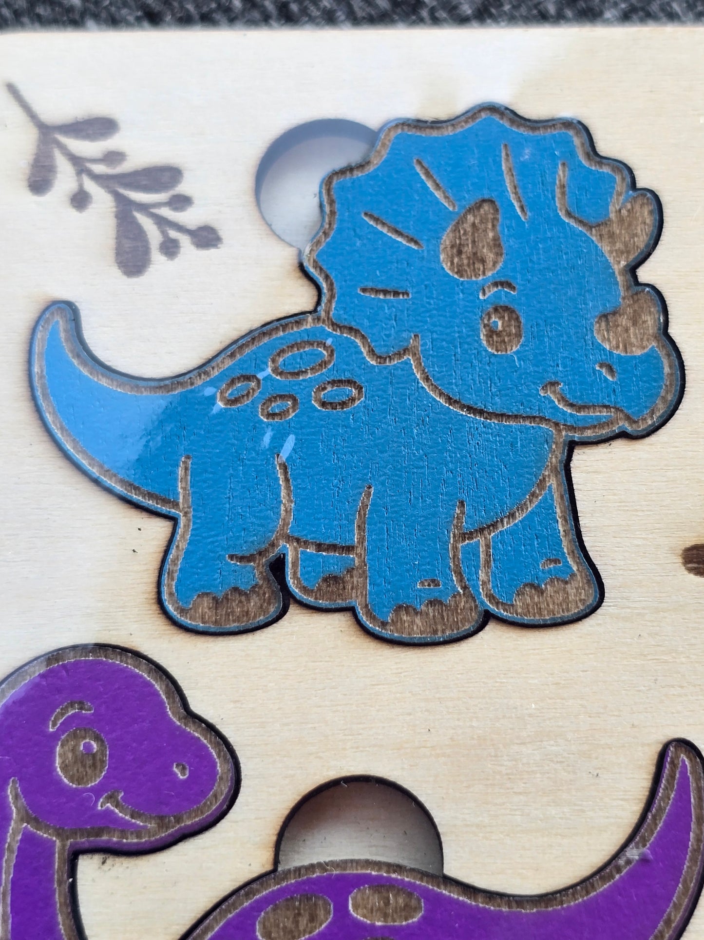 Decorative cut out shapes of a blue and purple dinosaur on a wooden surface.