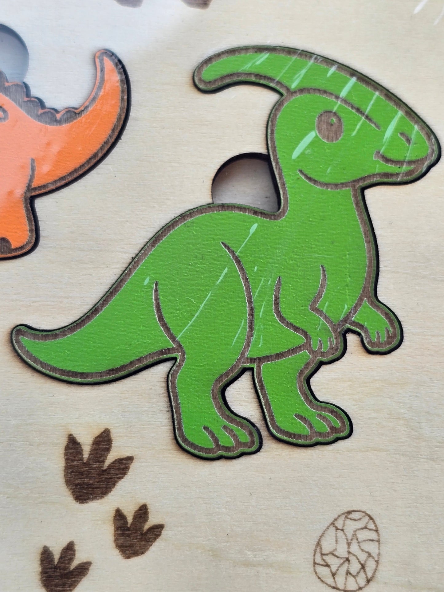 Green dinosaur-shaped puzzle piece on a wooden surface with other puzzle pieces.
