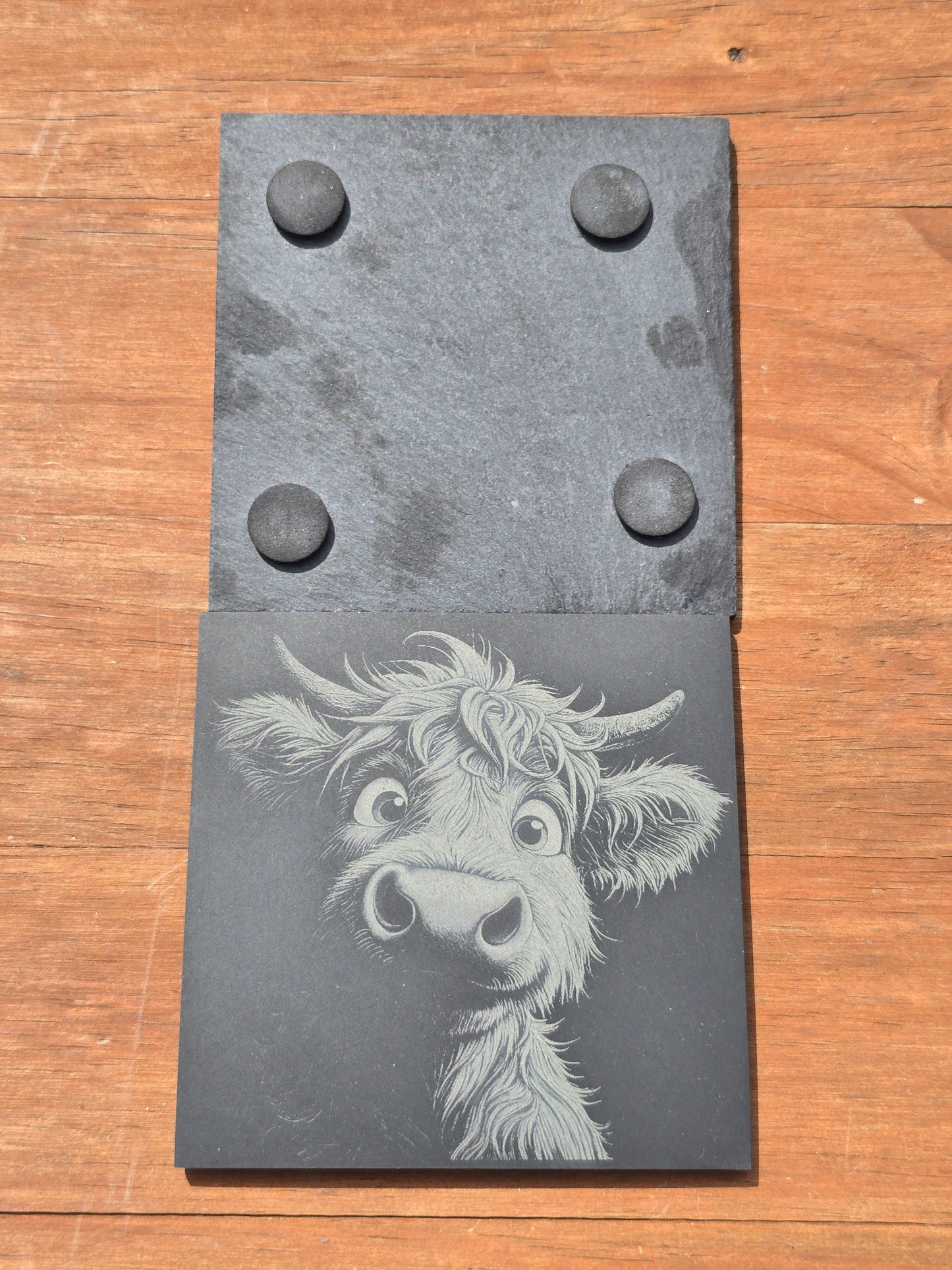 Front and back of a highland cow engraved slate, showing the felt feet on the bottom and etched design on the front