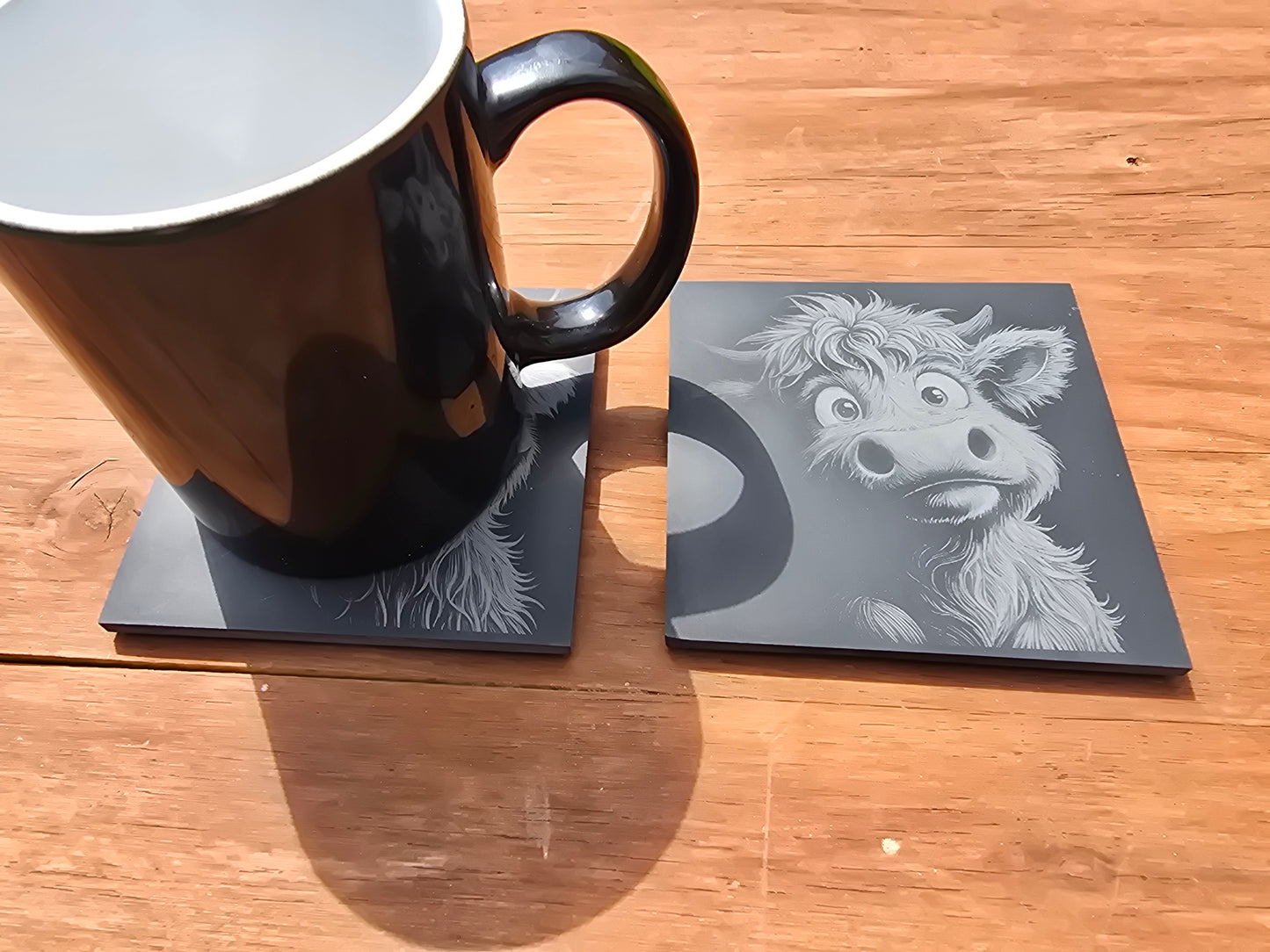 Black mug on a coaster with a baby highland cow design on a wooden table