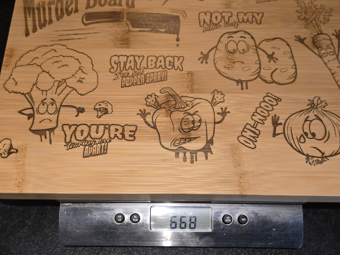 Wooden cutting board with engraved vegetable characters and a digital scale displaying a weight of 668g.