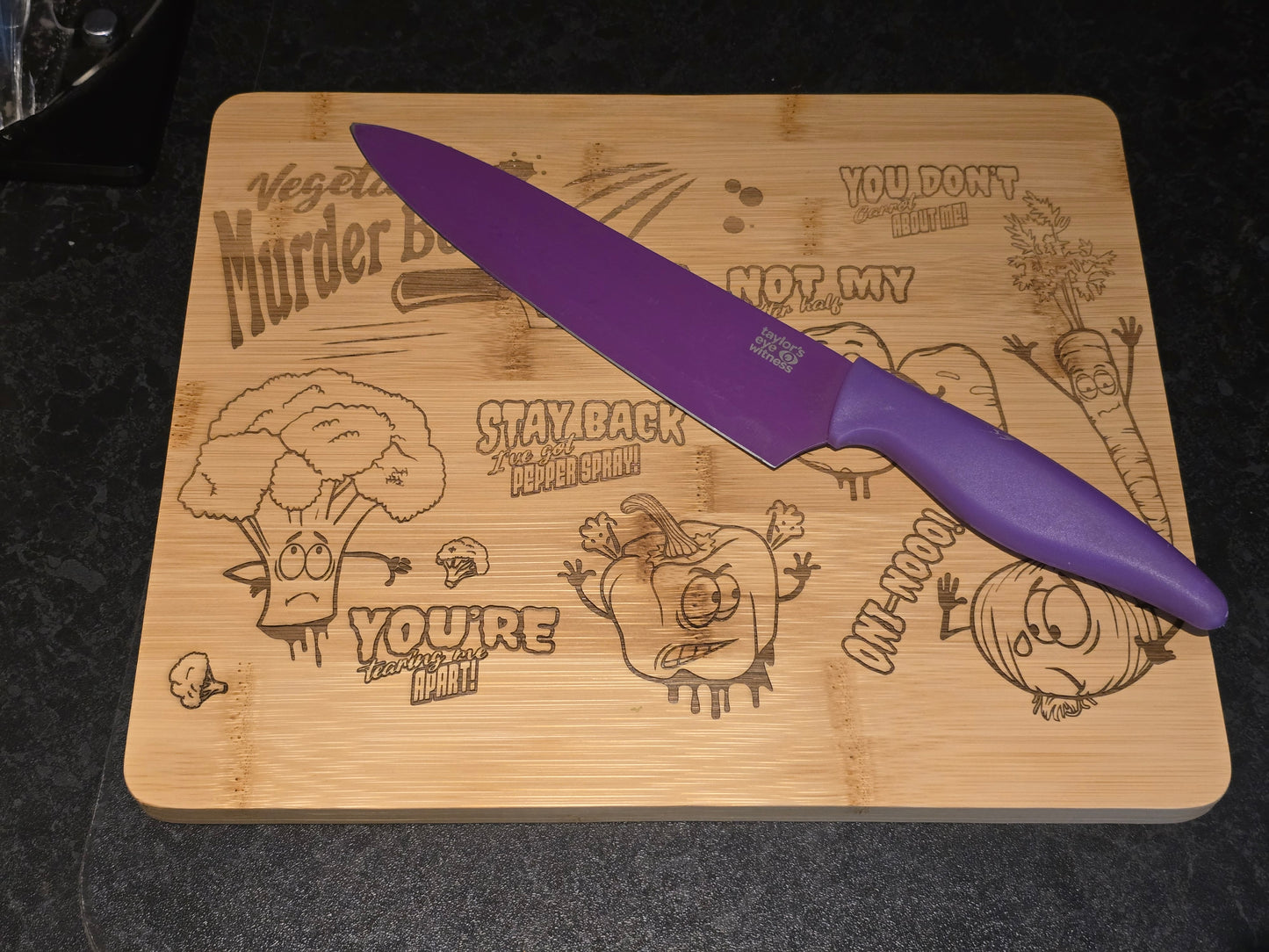 Purple knife on a wooden cutting board with cartoon vegetable designs