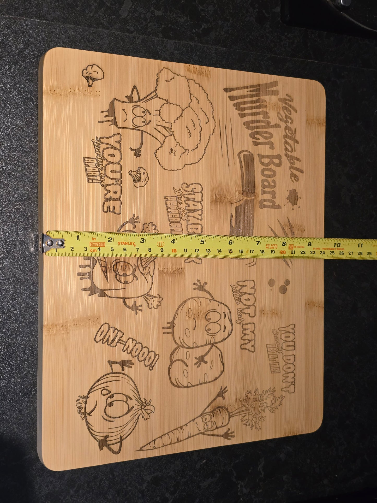 Wooden cutting board with vegetable-themed designs and a measuring tape showing 24cm width
