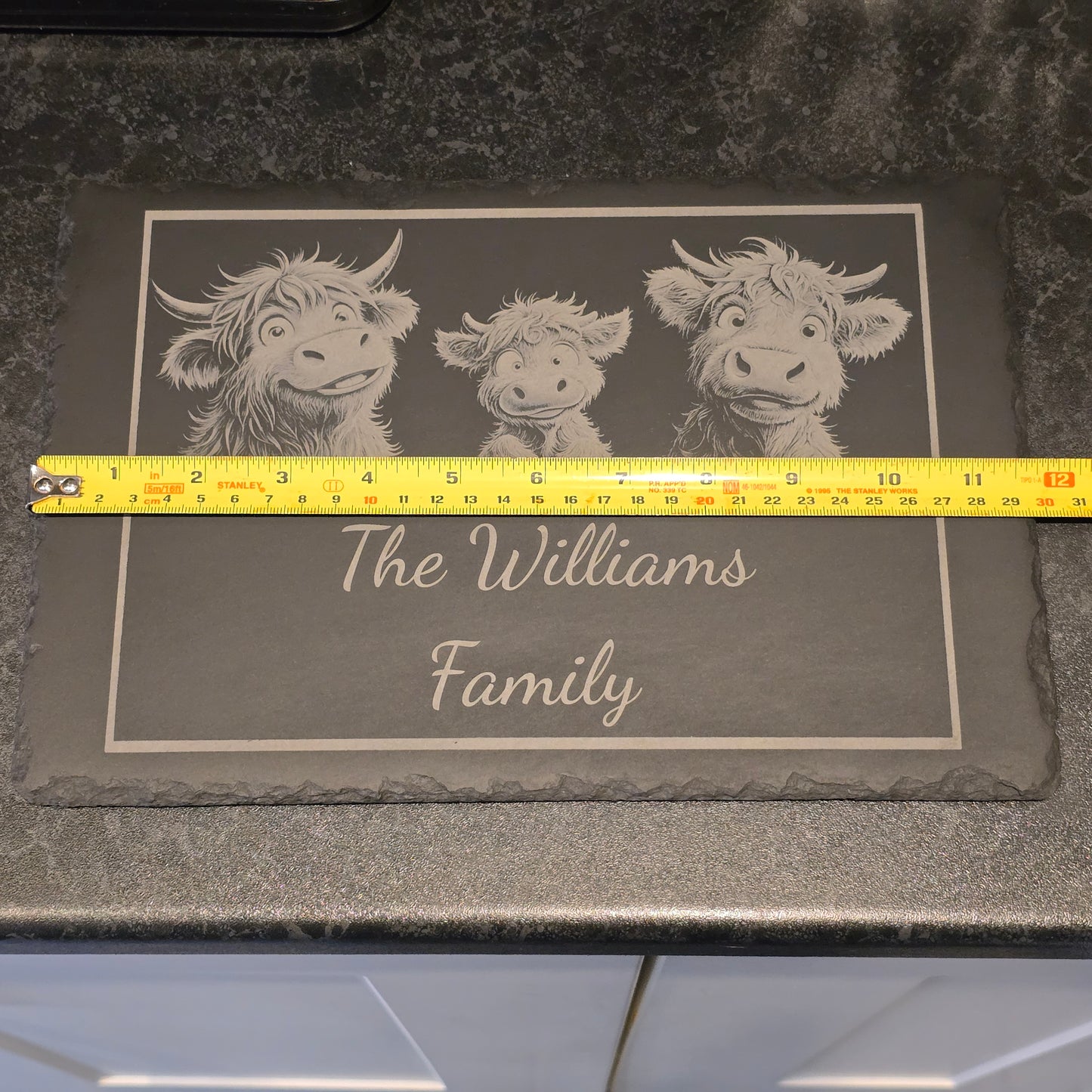 A family of highland cows engraved on a personalised cheese slate measuring 29cm in length