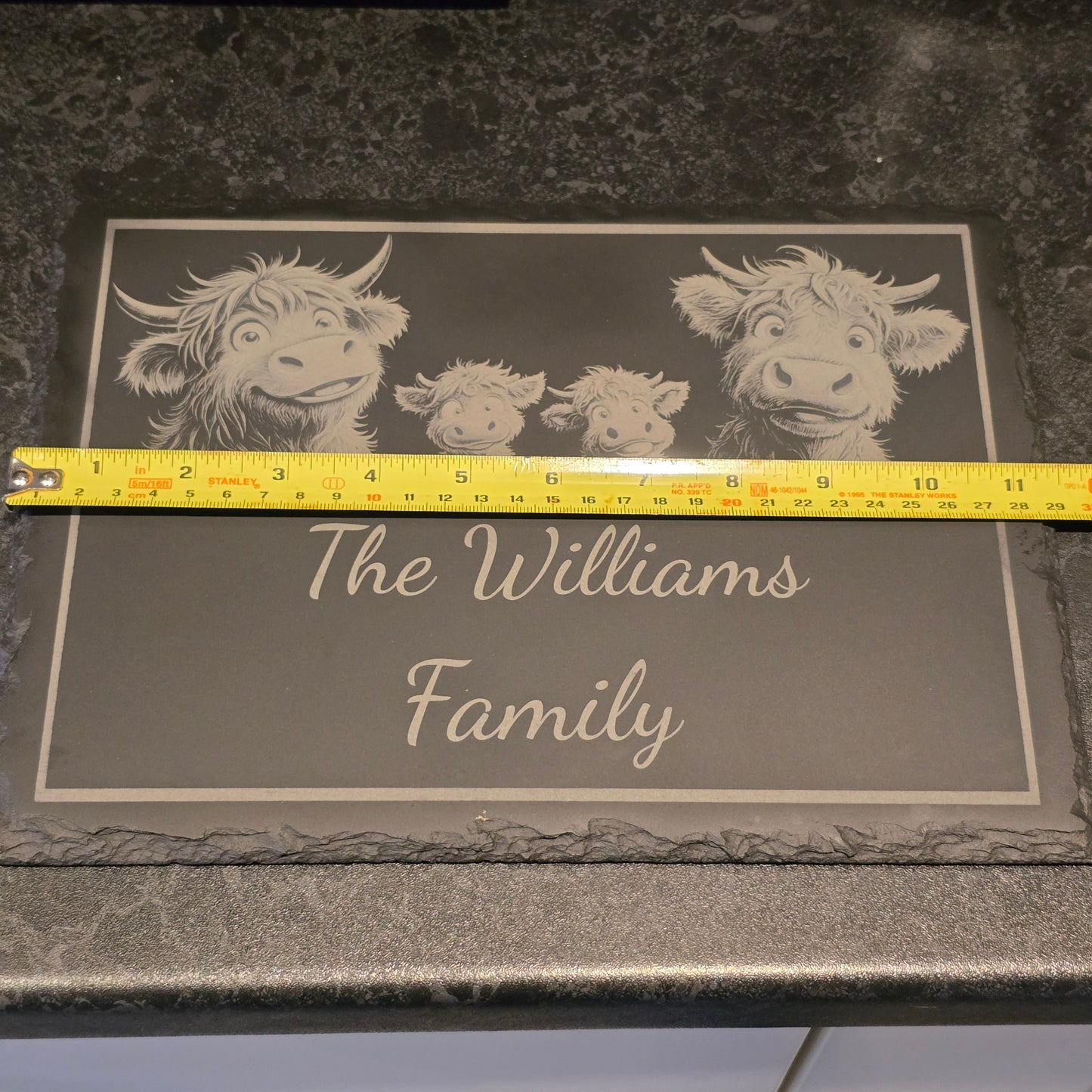 customised cheese slate with 'The Williams Family' text and highland cow illustrations, measured against a tape measure, shwing 29cm