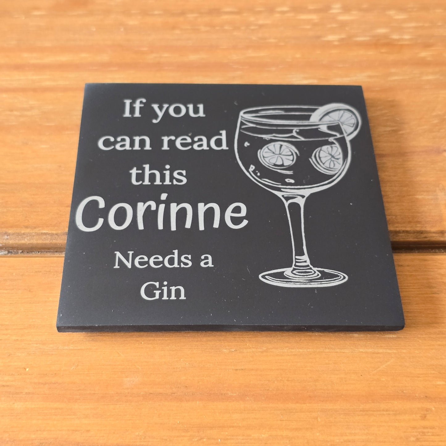Black coaster with white text and gin glass illustration on a wooden surface