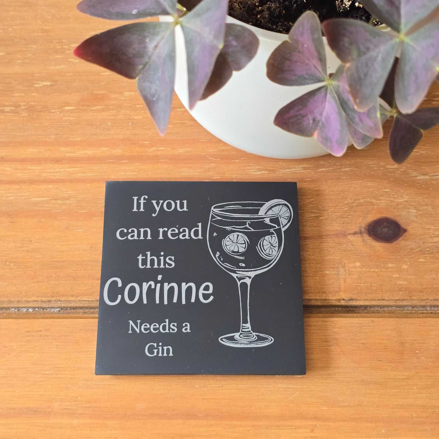 Personalized slate coaster with a gin glass illustration and text on a wooden surface with a plant.
