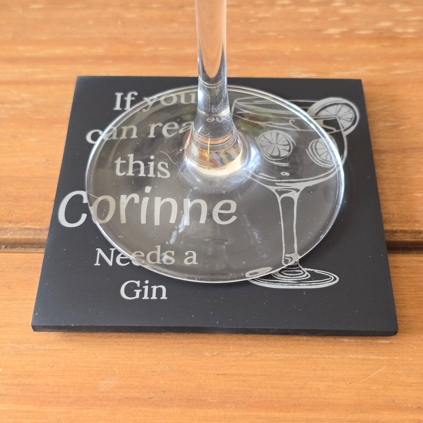 Glass of gin on a personalised coaster with text on a wooden surface