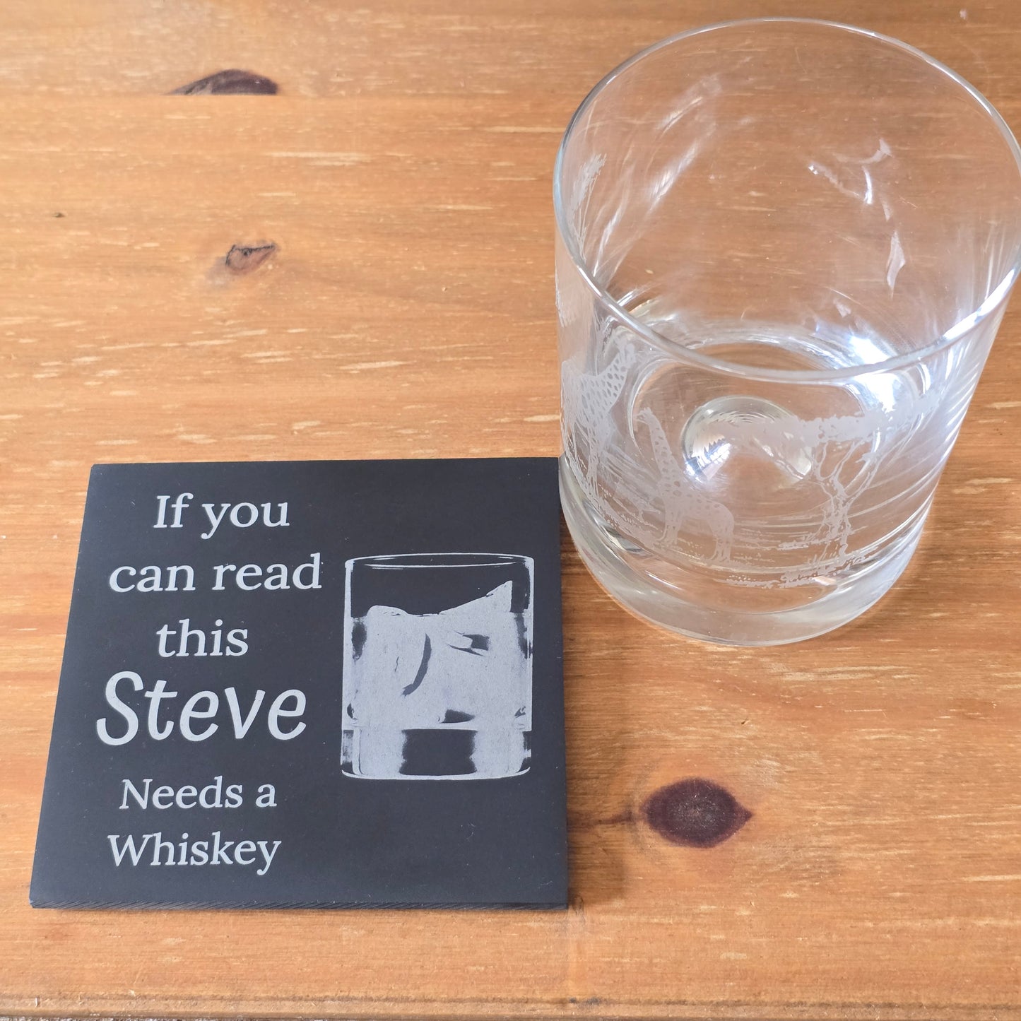 Whiskey glass and a personalised coaster with text on a wooden surface