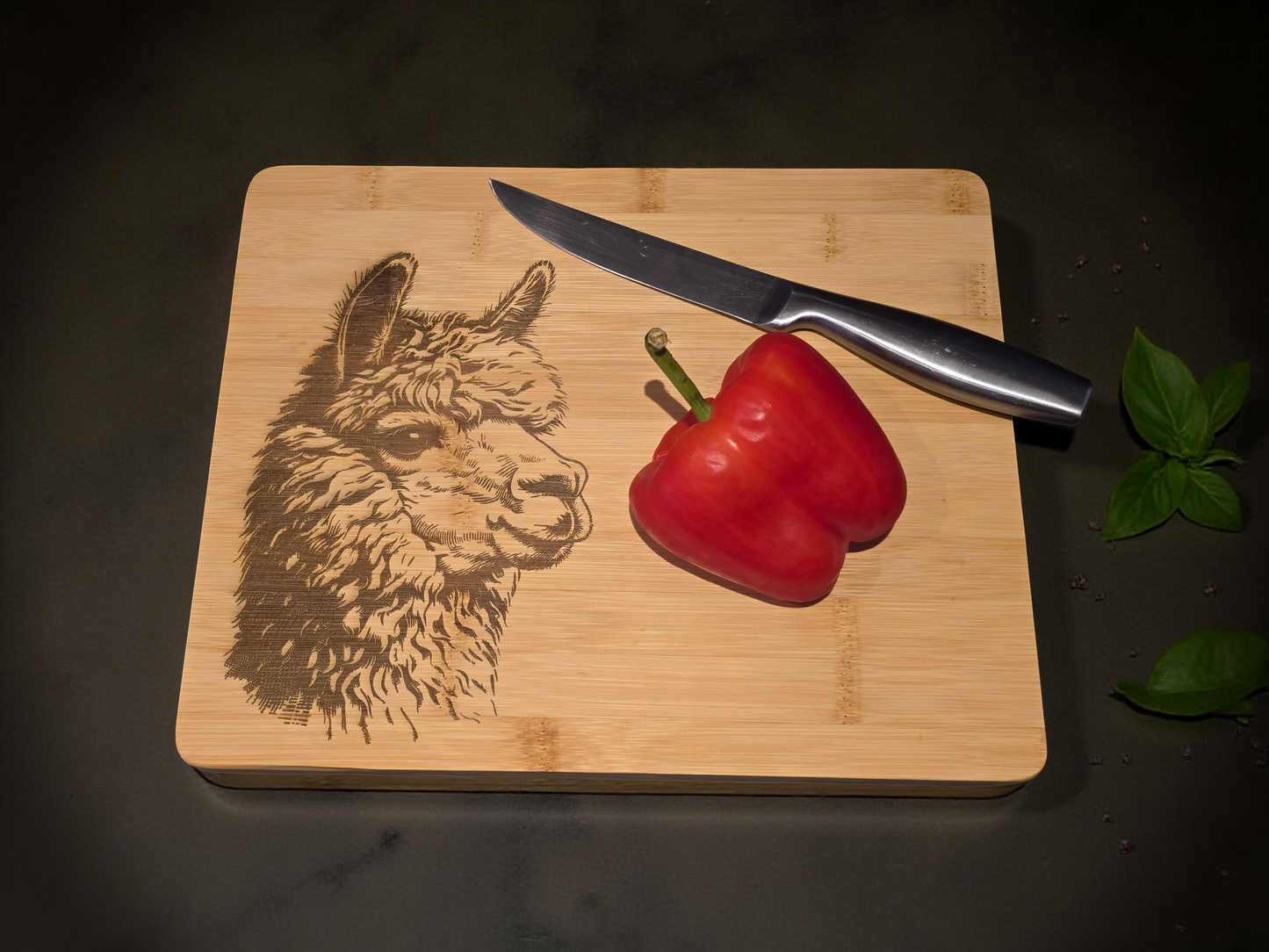 Wooden cutting board with engraved alpaca design, knife, and red pepper on a dark surface