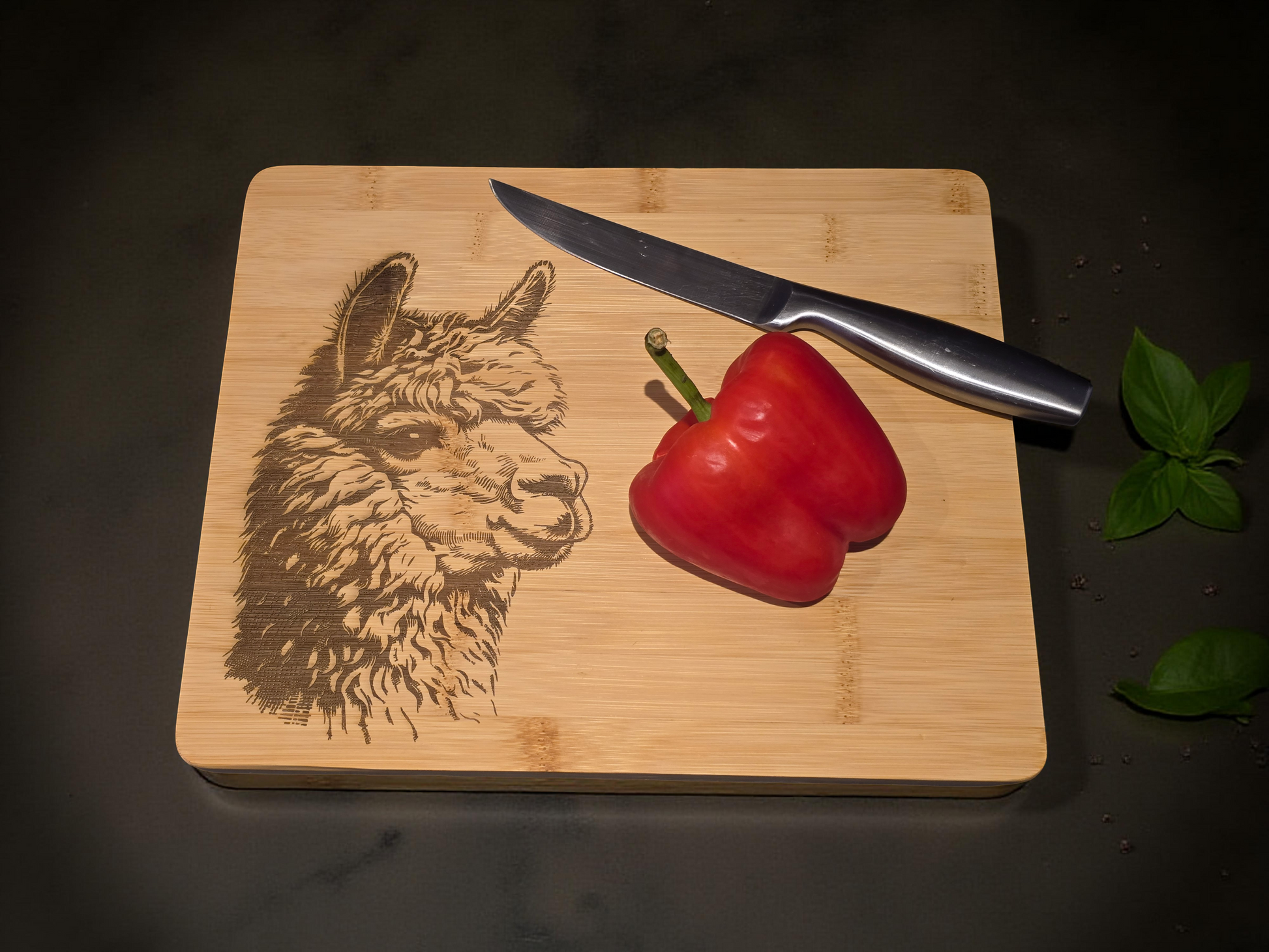Wooden cutting board with engraved alpaca design, knife, and red pepper on a dark surface