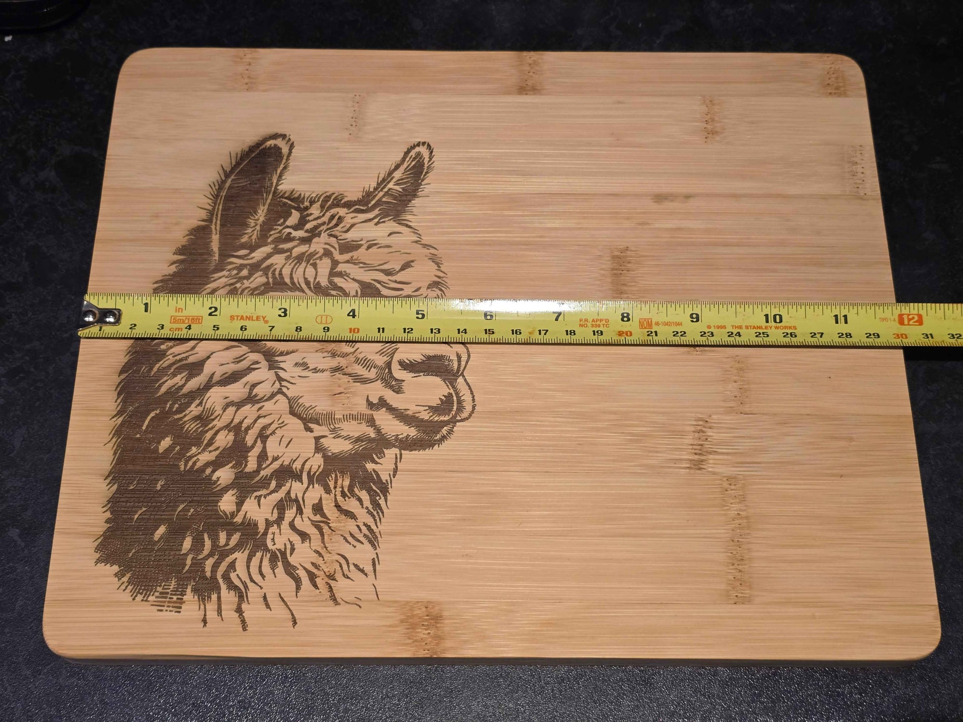 Wooden cutting board with a engraved alpaca design and a measuring tape for scale. showing 30cm length.