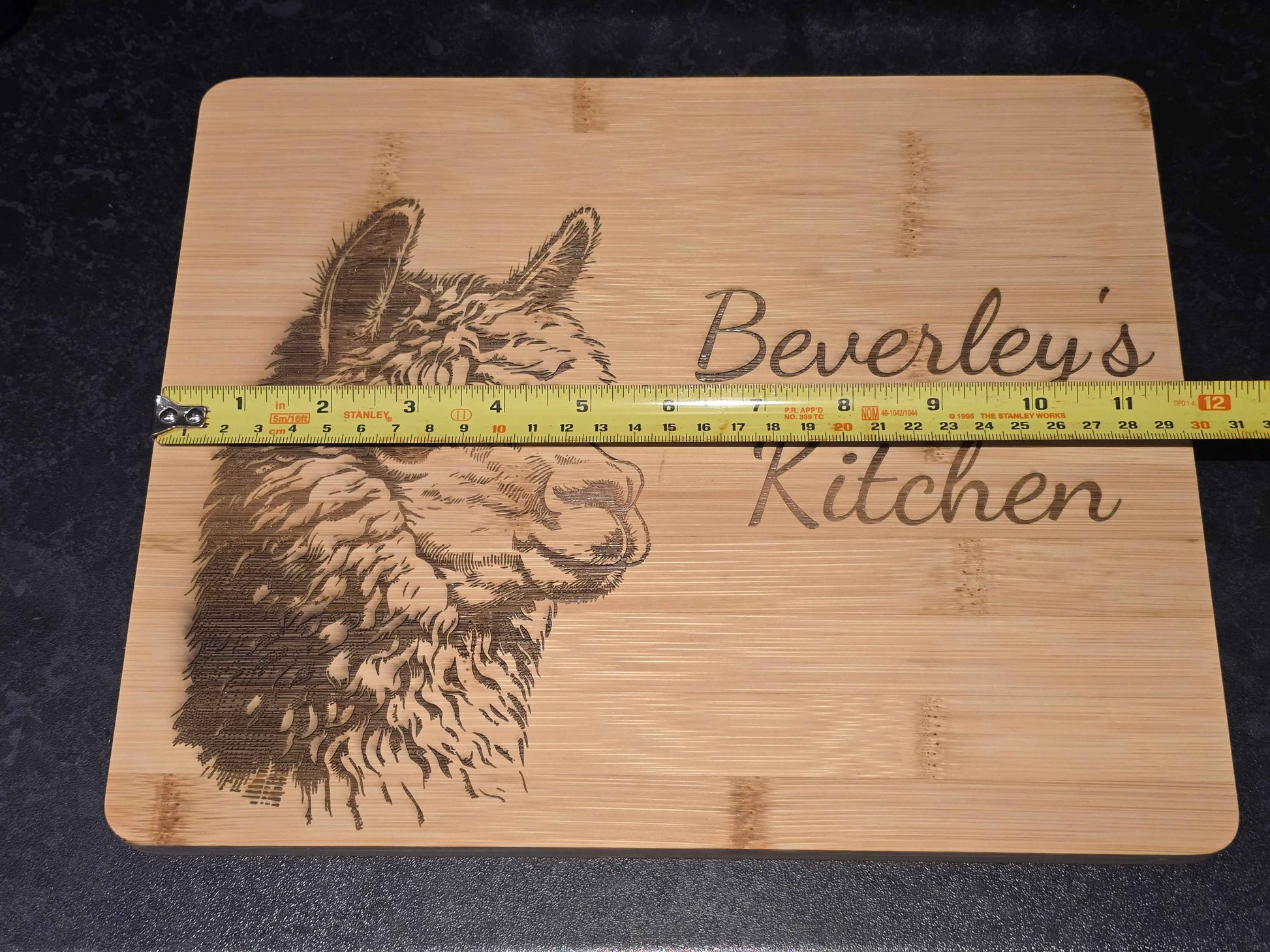 Bamboo cutting board with engraved alpaca design and 'Beverley's Kitchen' text, measured by a ruler showing 30cm length