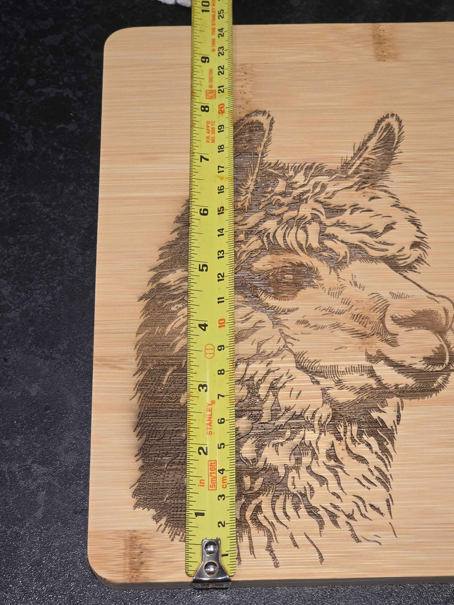 Wooden cutting board with a engraved alpaca design and a tape measure for scale, displaying 24cm width