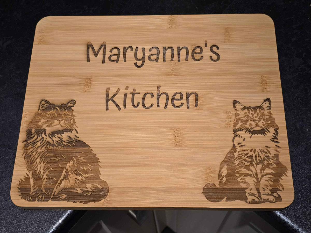 Bamboo cutting board with engraved cat illustrations and custom name text on a kitchen counter