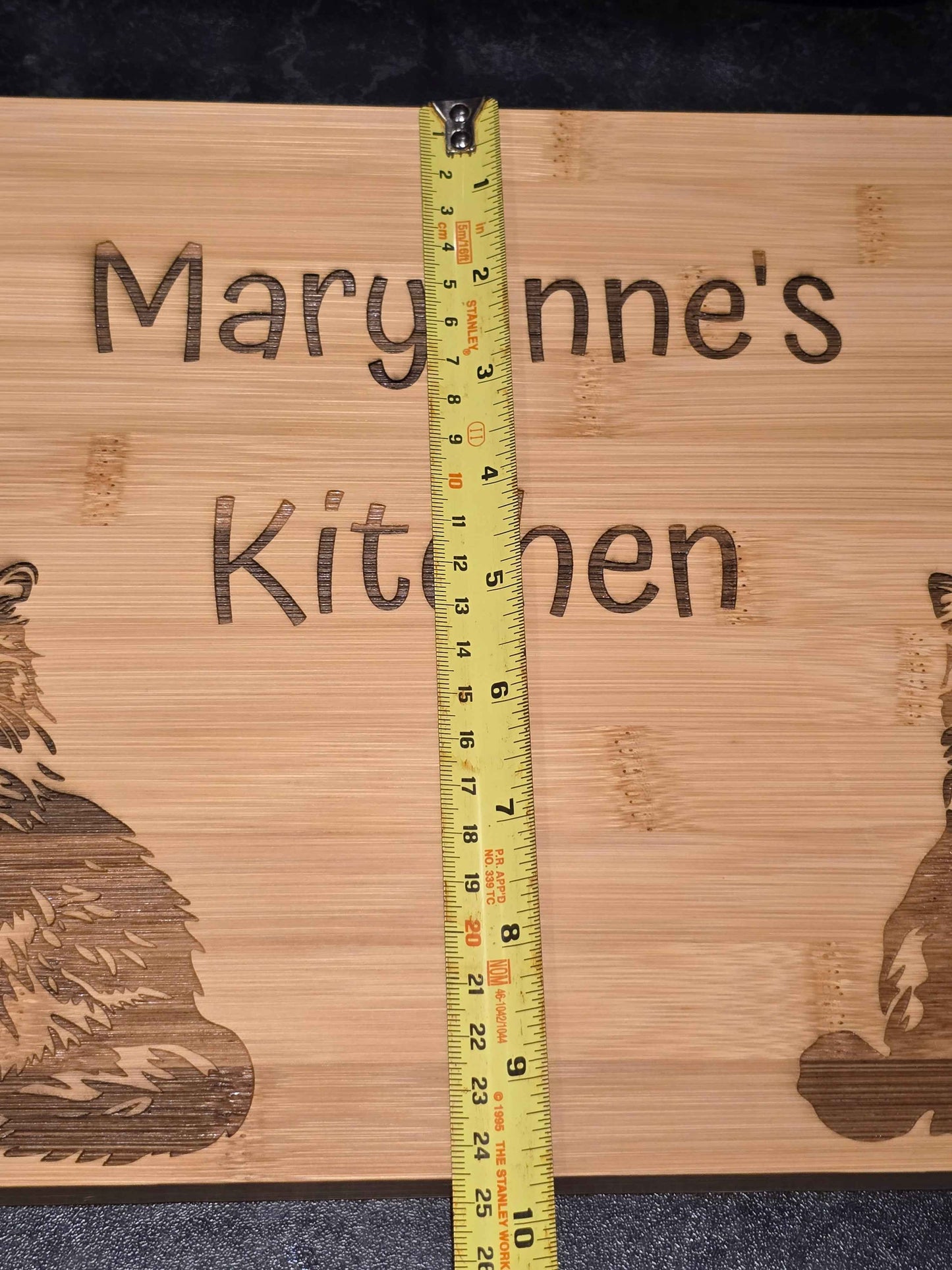 Bamboo cutting board with engraved text and cat illustrations, featuring a measuring tape for scale showing 24cm width