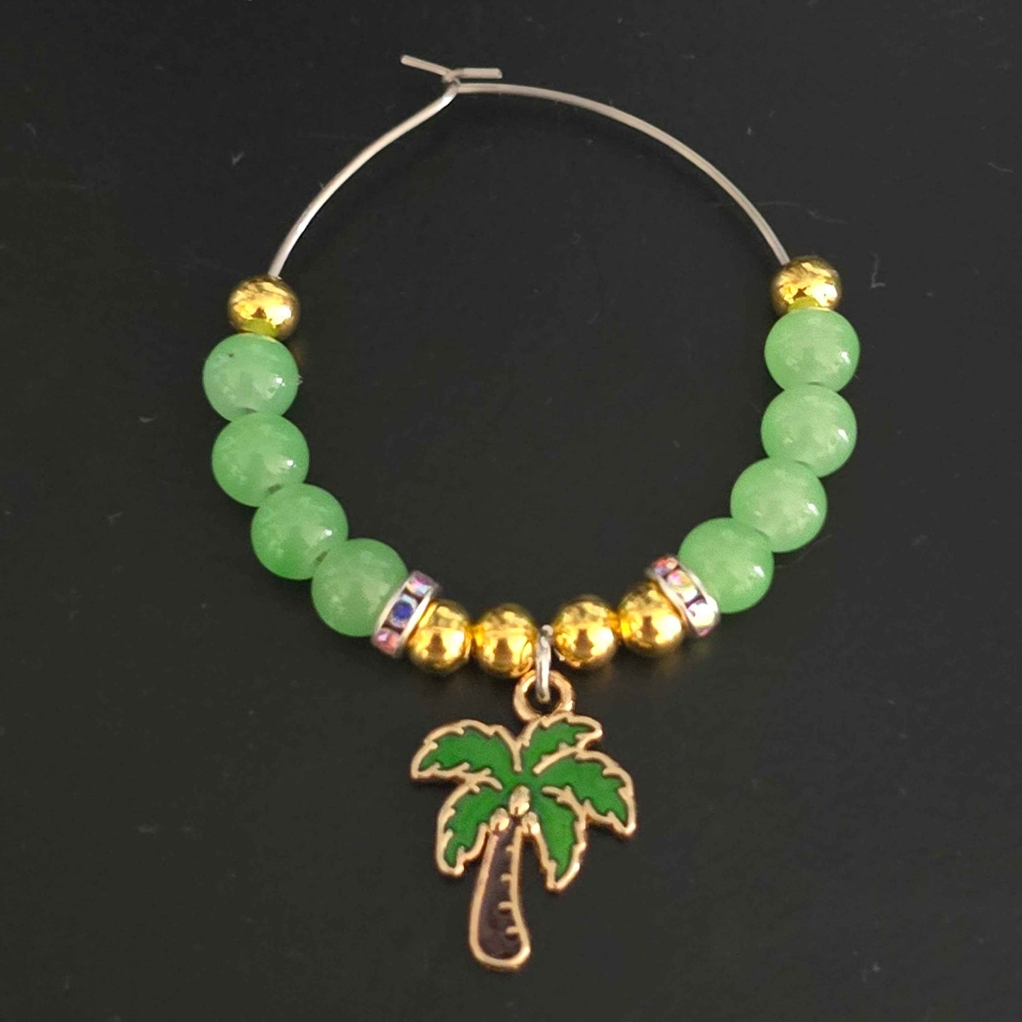 top down shot of a tropical themed wine glass charm with a palm tree charm, green and gold beads
