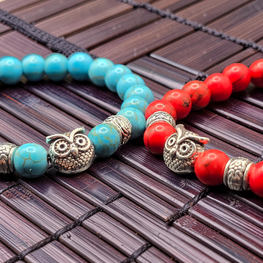 Two beaded bracelets with owl charms on a wooden surface